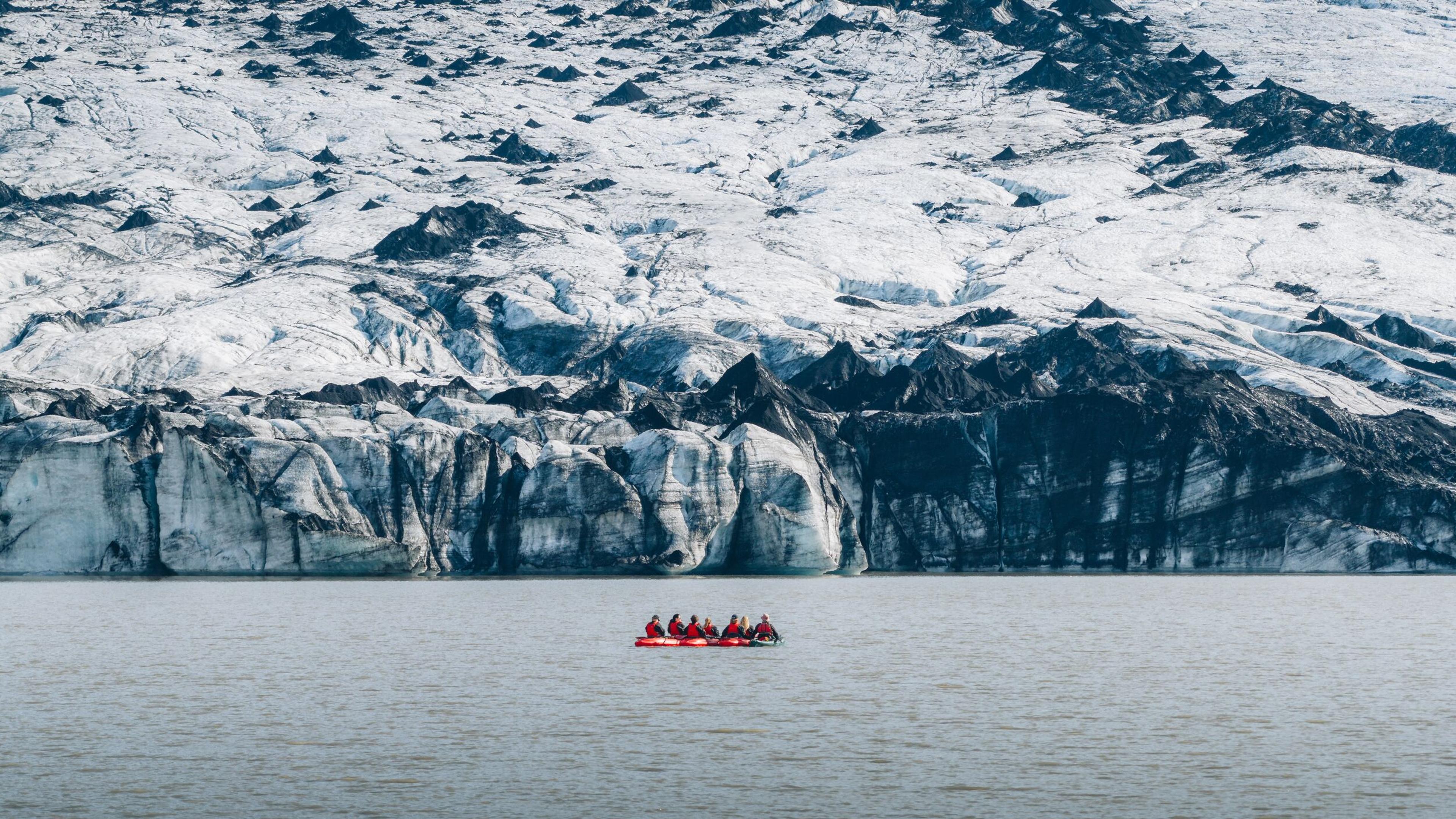 A man on a red kayak paddling through some ice bergs.