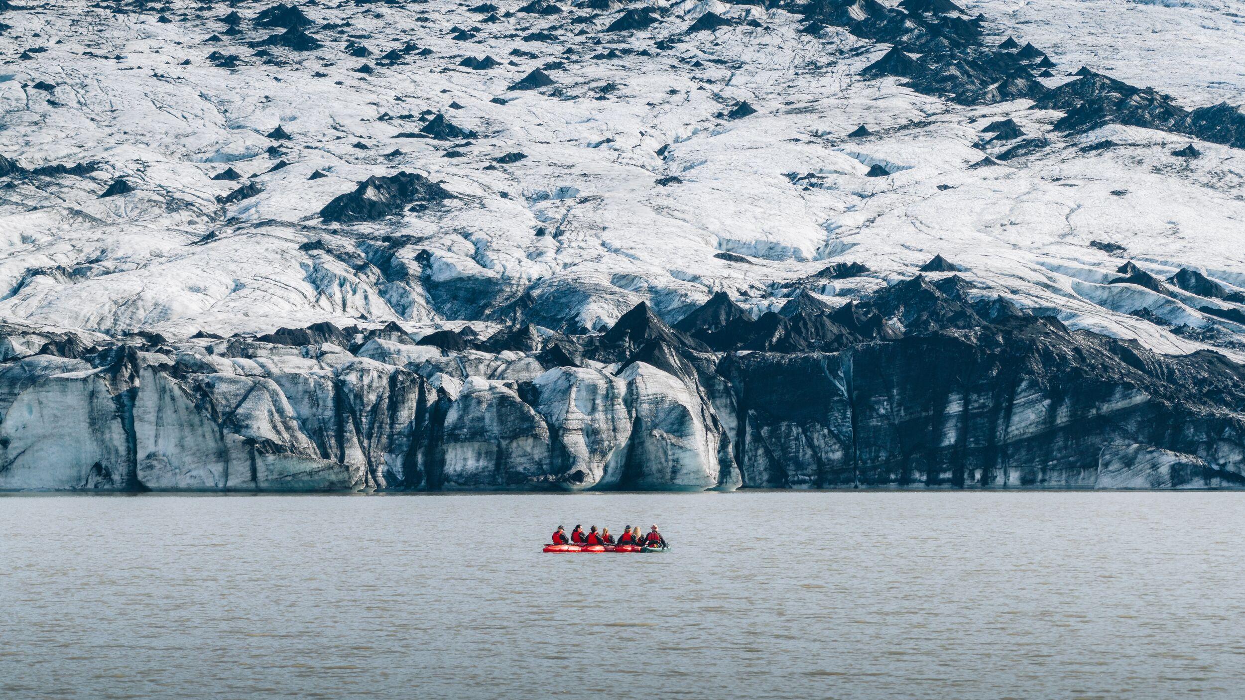 A man on a red kayak paddling through some ice bergs.