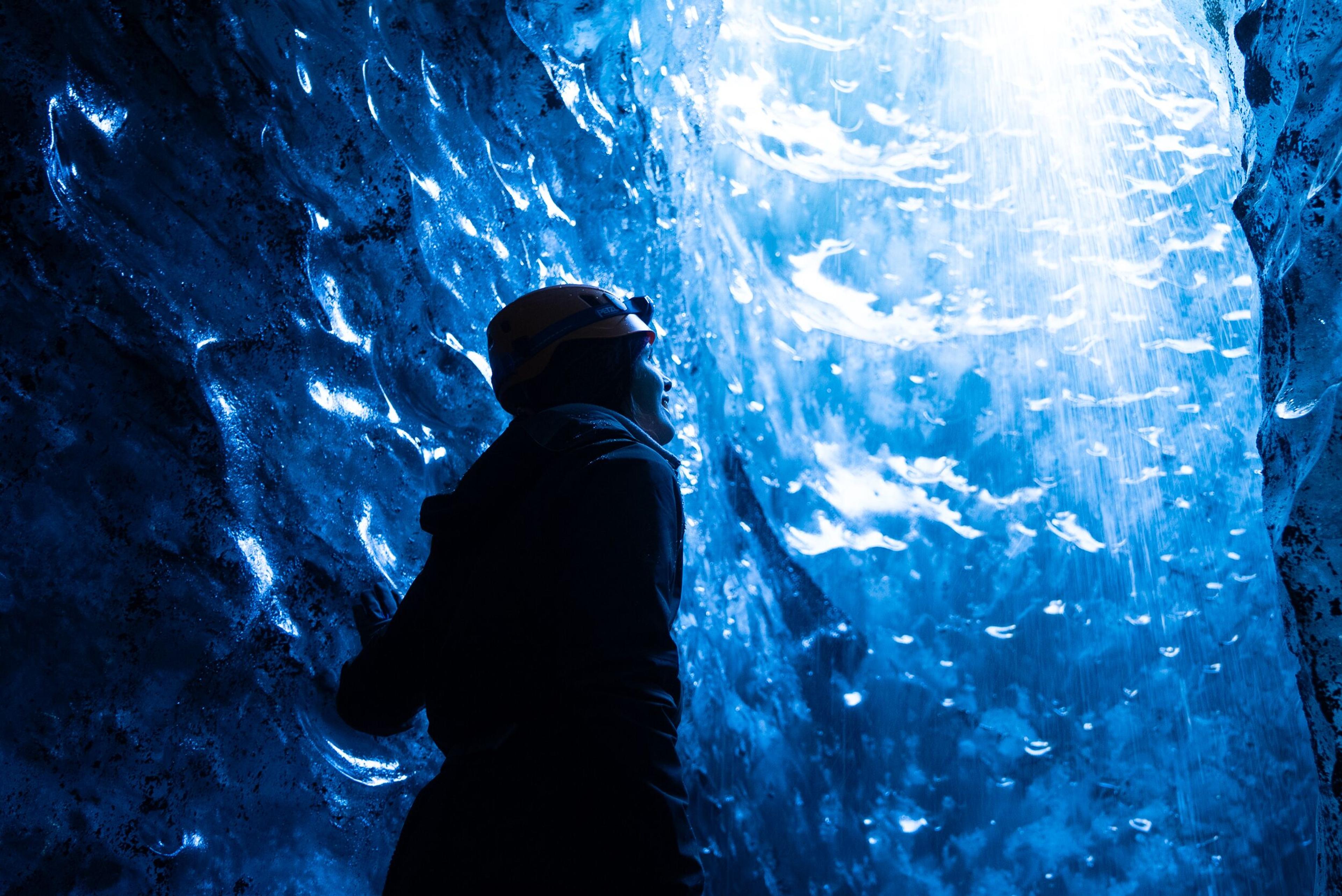 A woman stood in an ice cave looking up at the light coming in from above