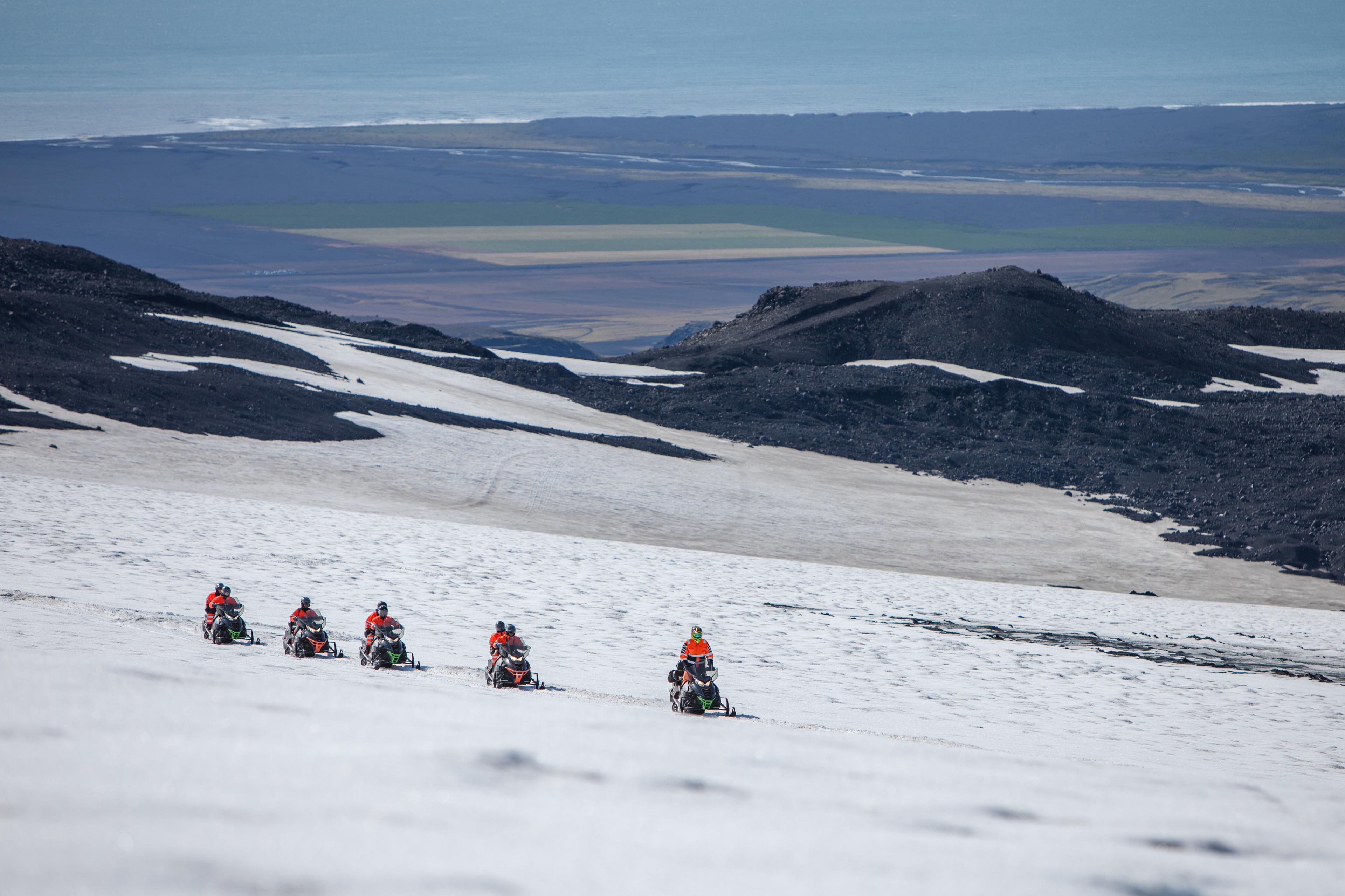 Group of snow scooter riders on the glacier and a view of the lowlands in the background