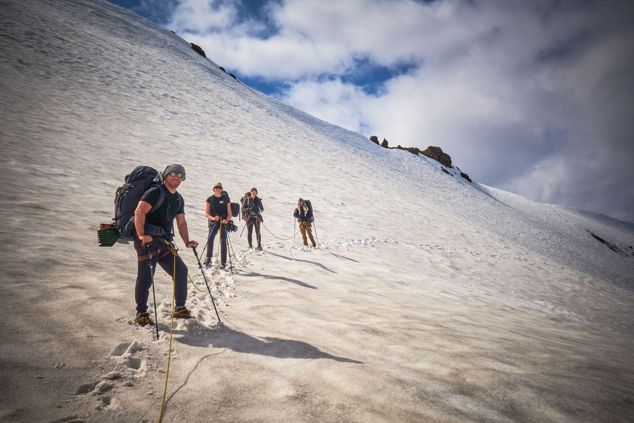 Four hikers in a line going over a glacier in their t-shirts