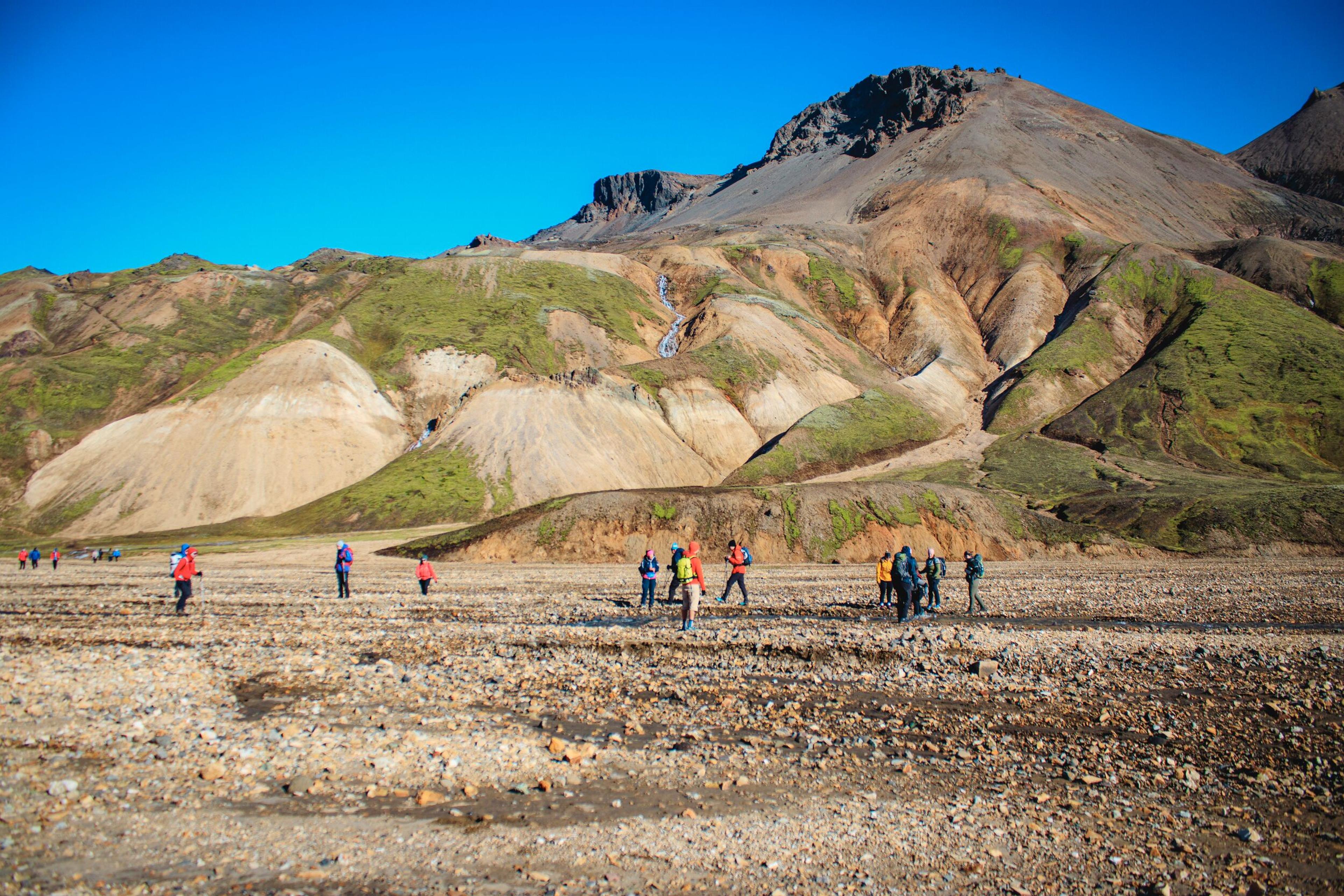 People hiking on gravel with brown and green mountain