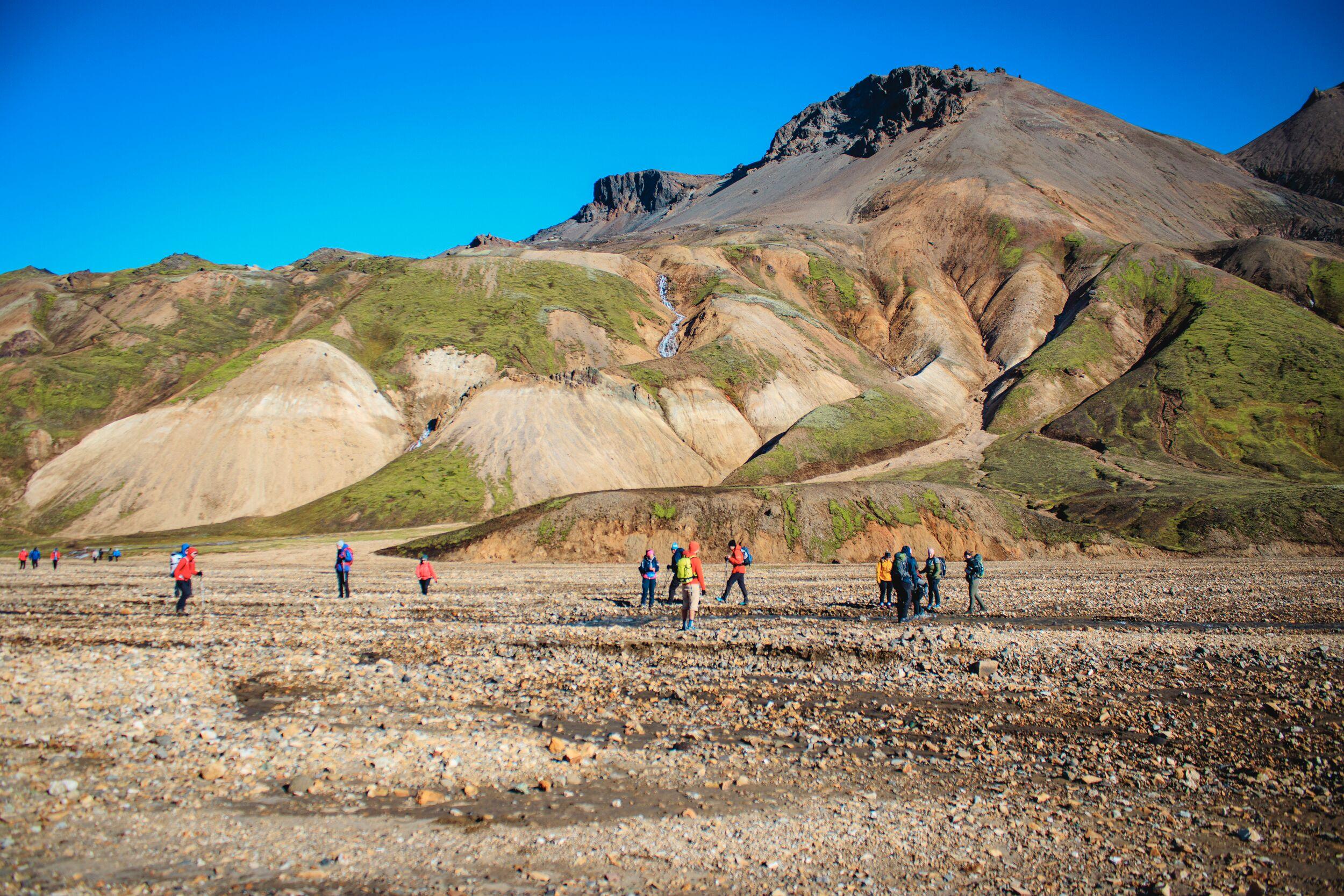 People hiking on gravel with brown and green mountain