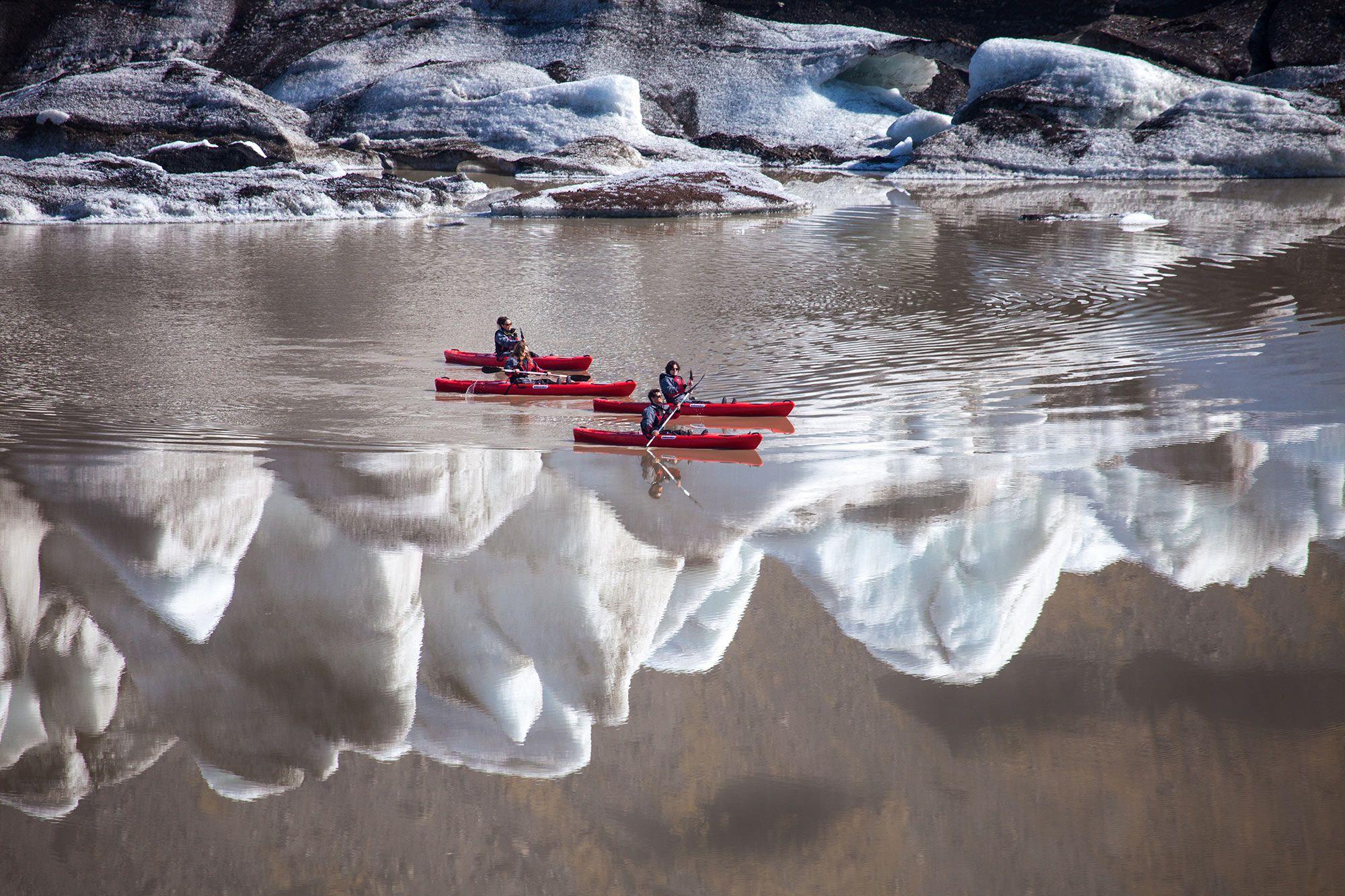 A man on a red kayak paddling through some ice bergs.