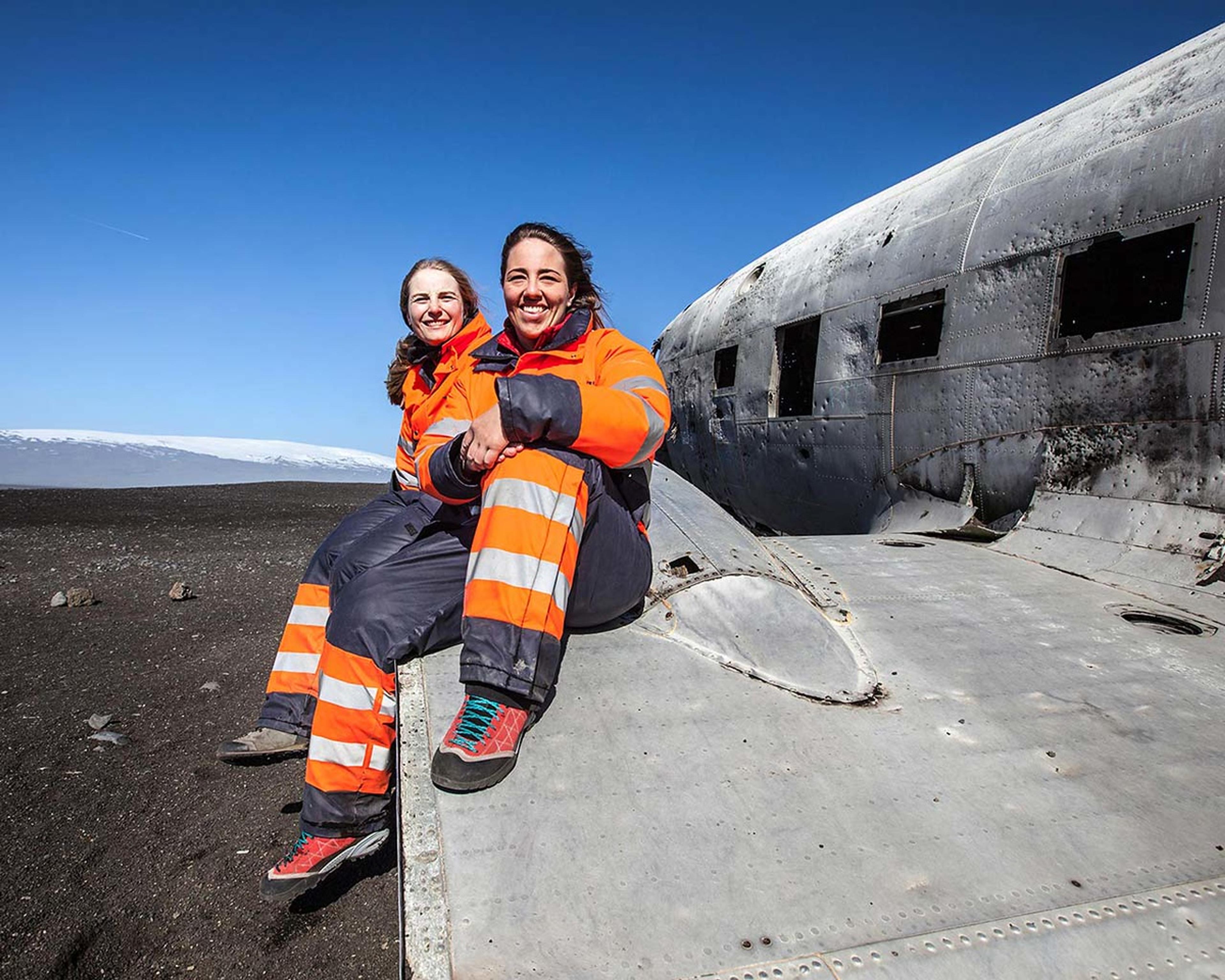 Two girls sitting on the wing of the old DC3 plane wreck stuck in the sand