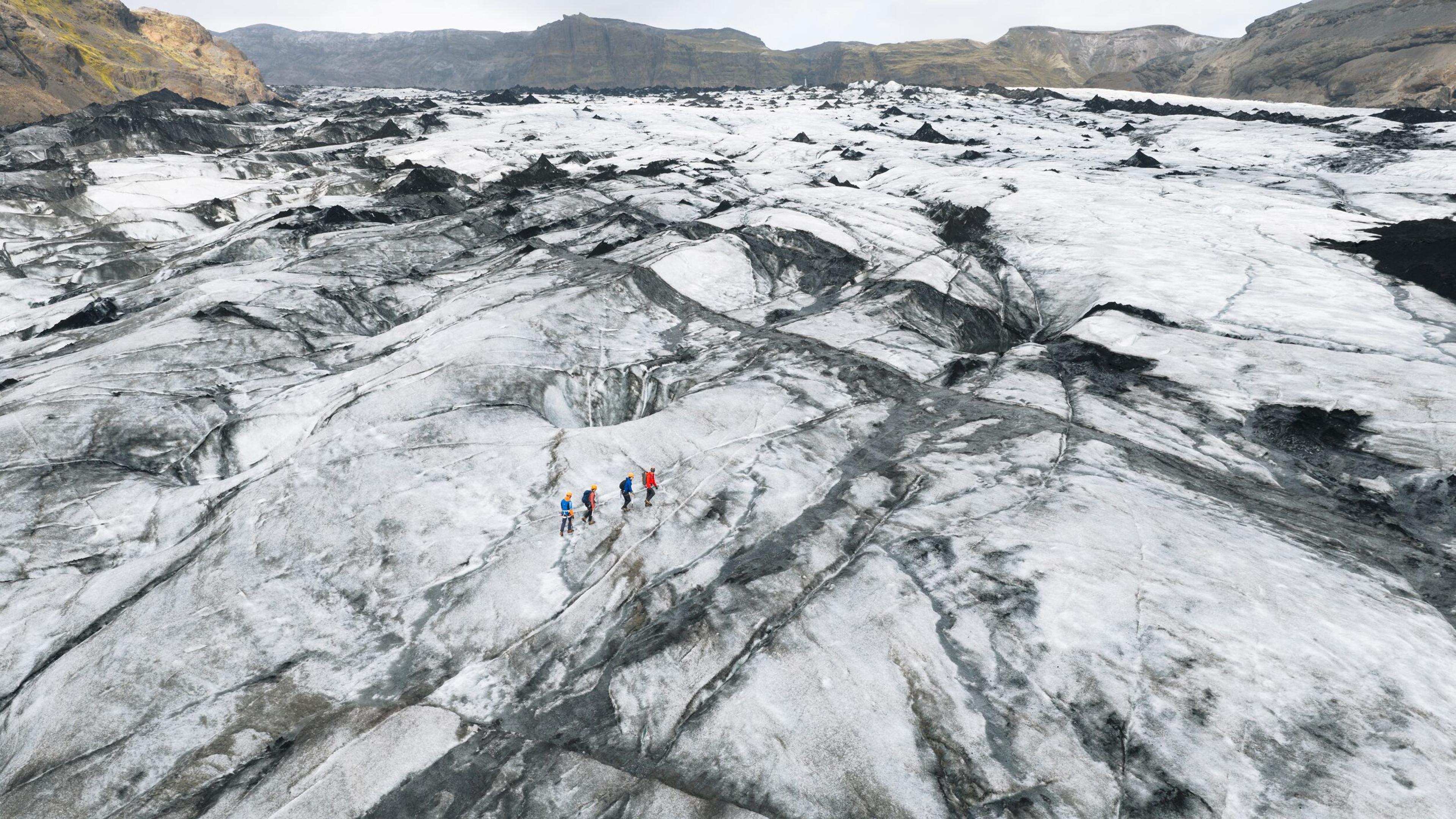 four persons walking on a glacier 