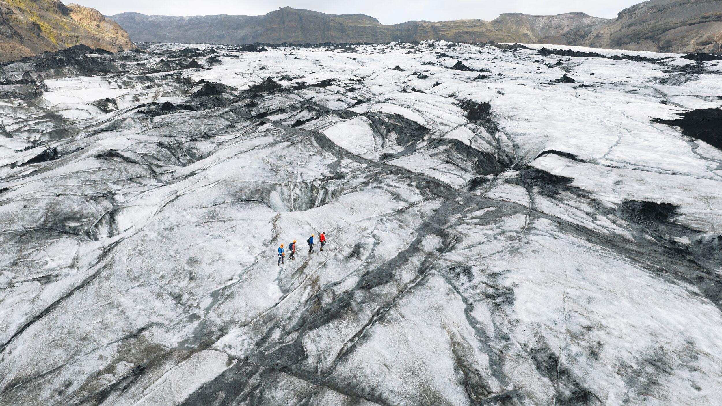 four persons walking on a glacier