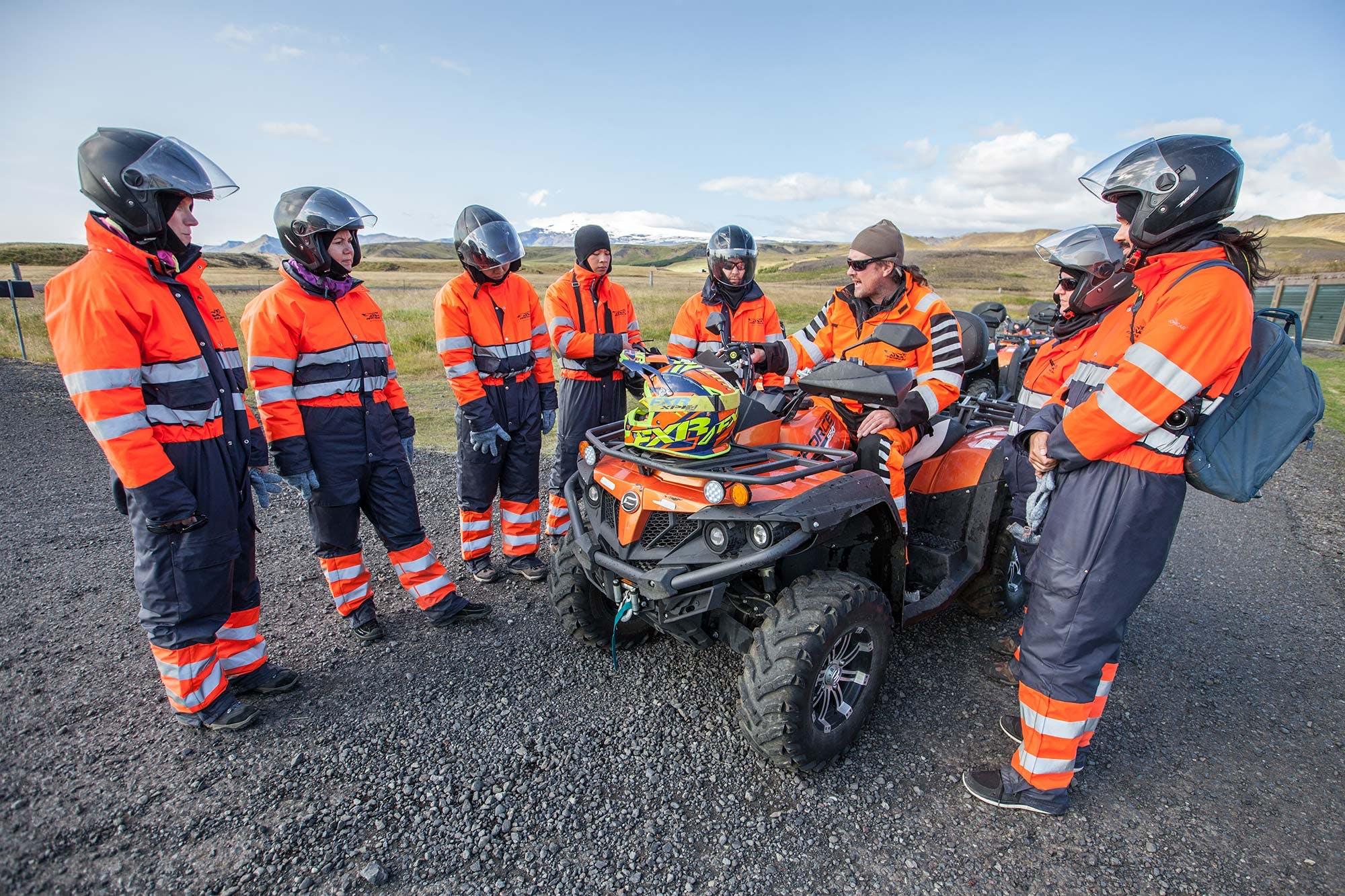 A group of people dressed in coveralls with helmets standing around a guide on an ATV preparing for a tour