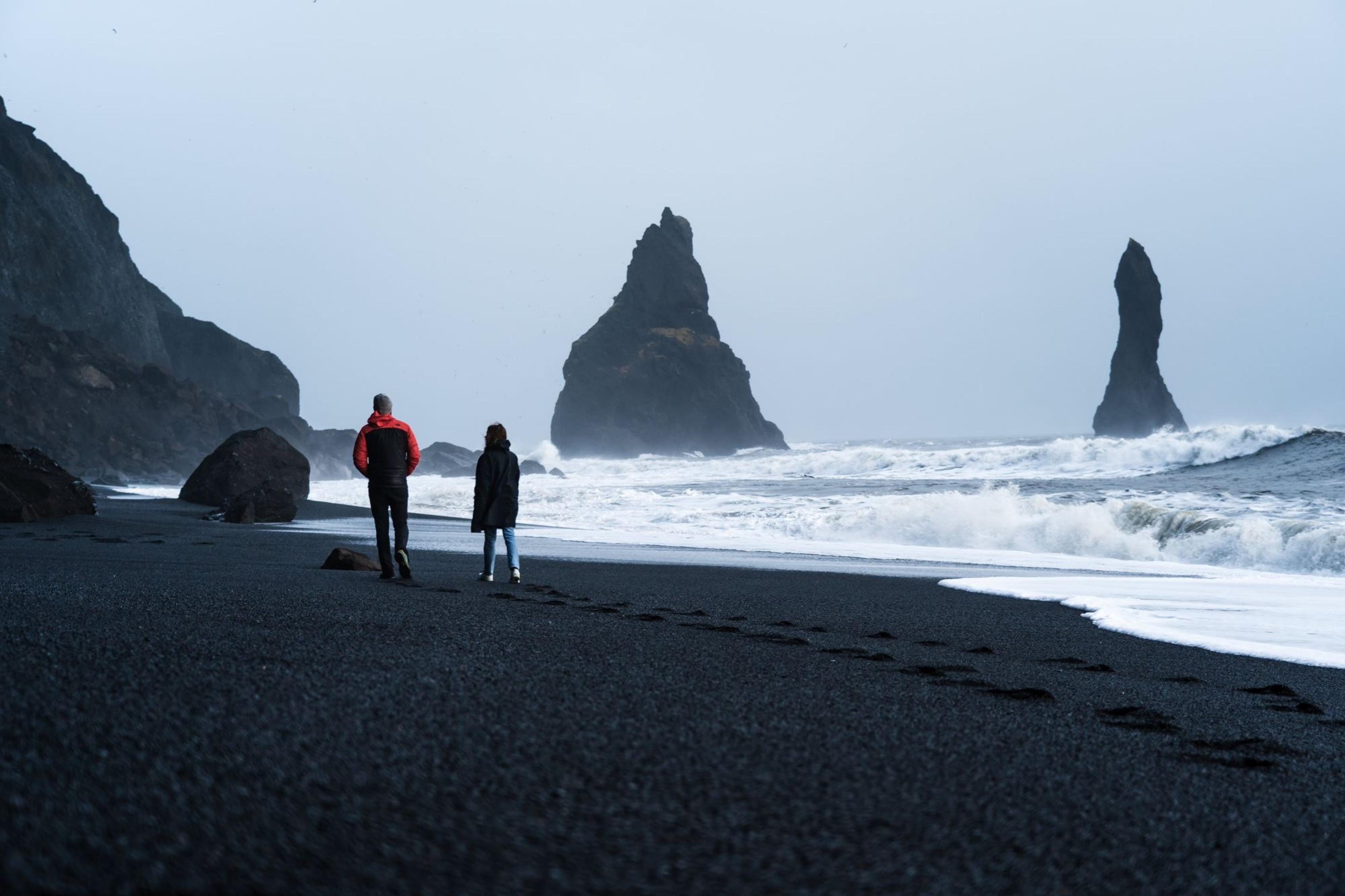 Two people walking along Reynisfjara shoreline