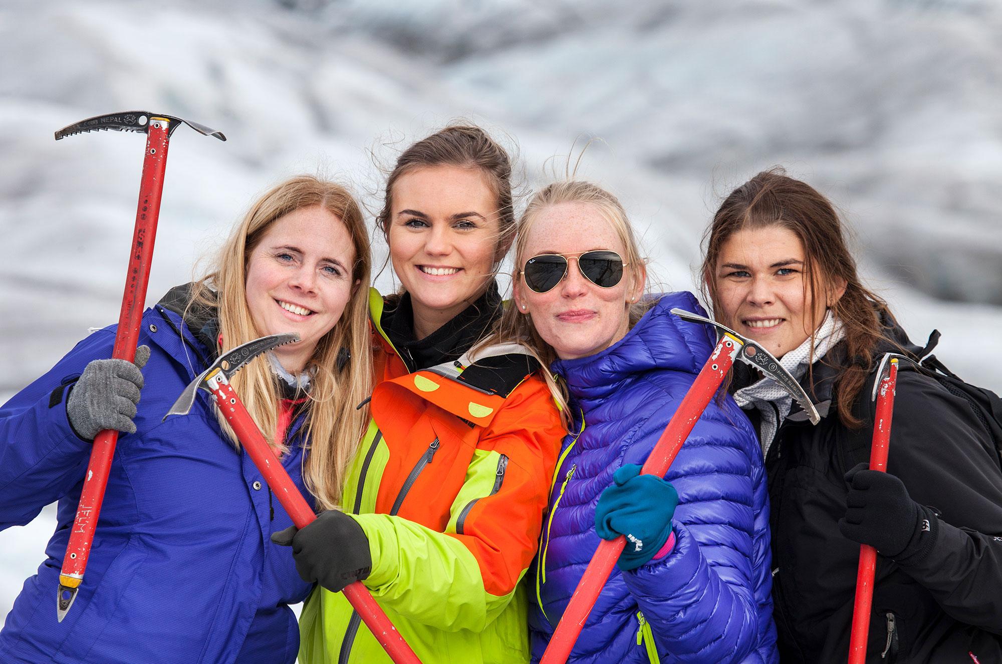 A group of smiling women holding ice axes while on a glacier in Iceland.
