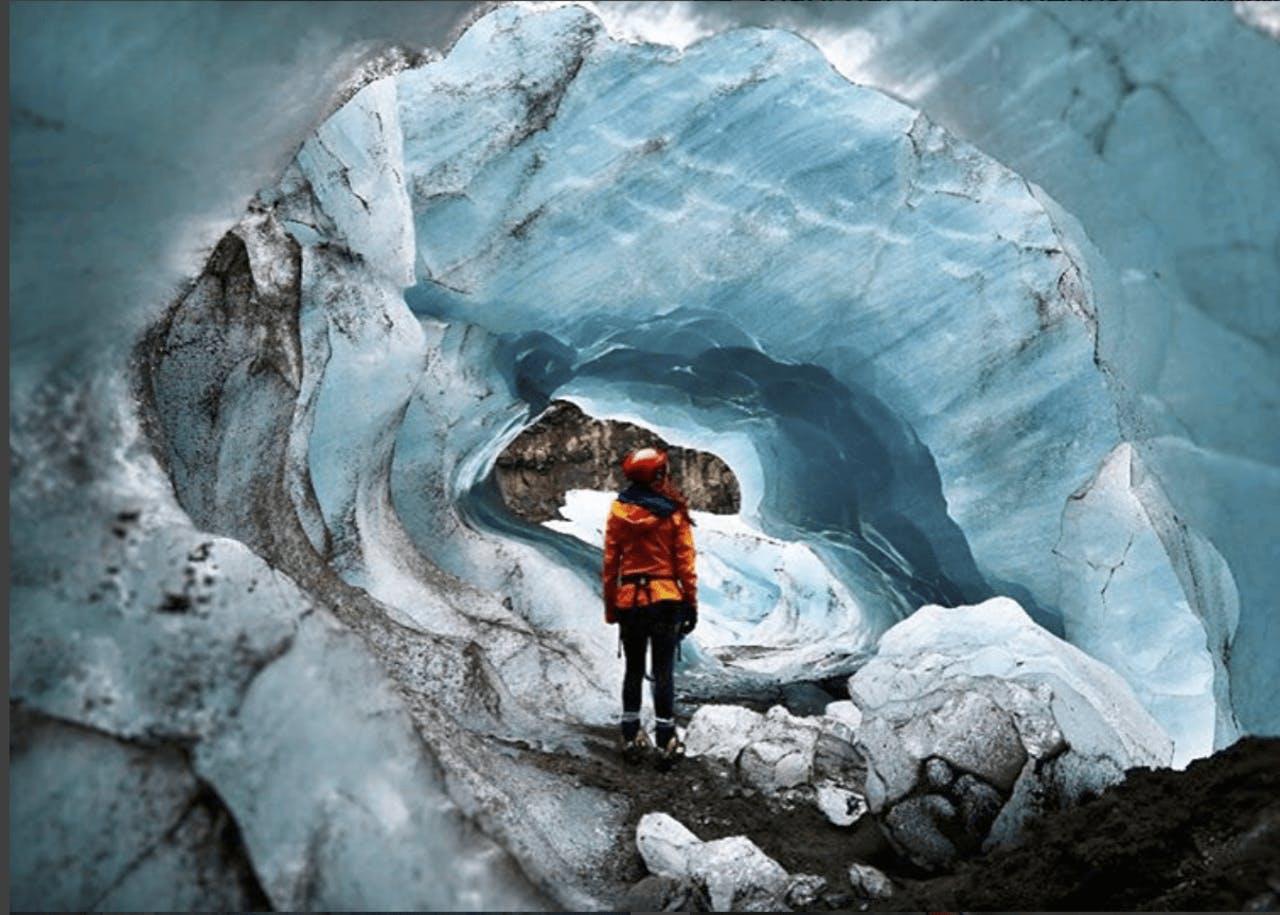 woman in an orange coat standing in an ice cave