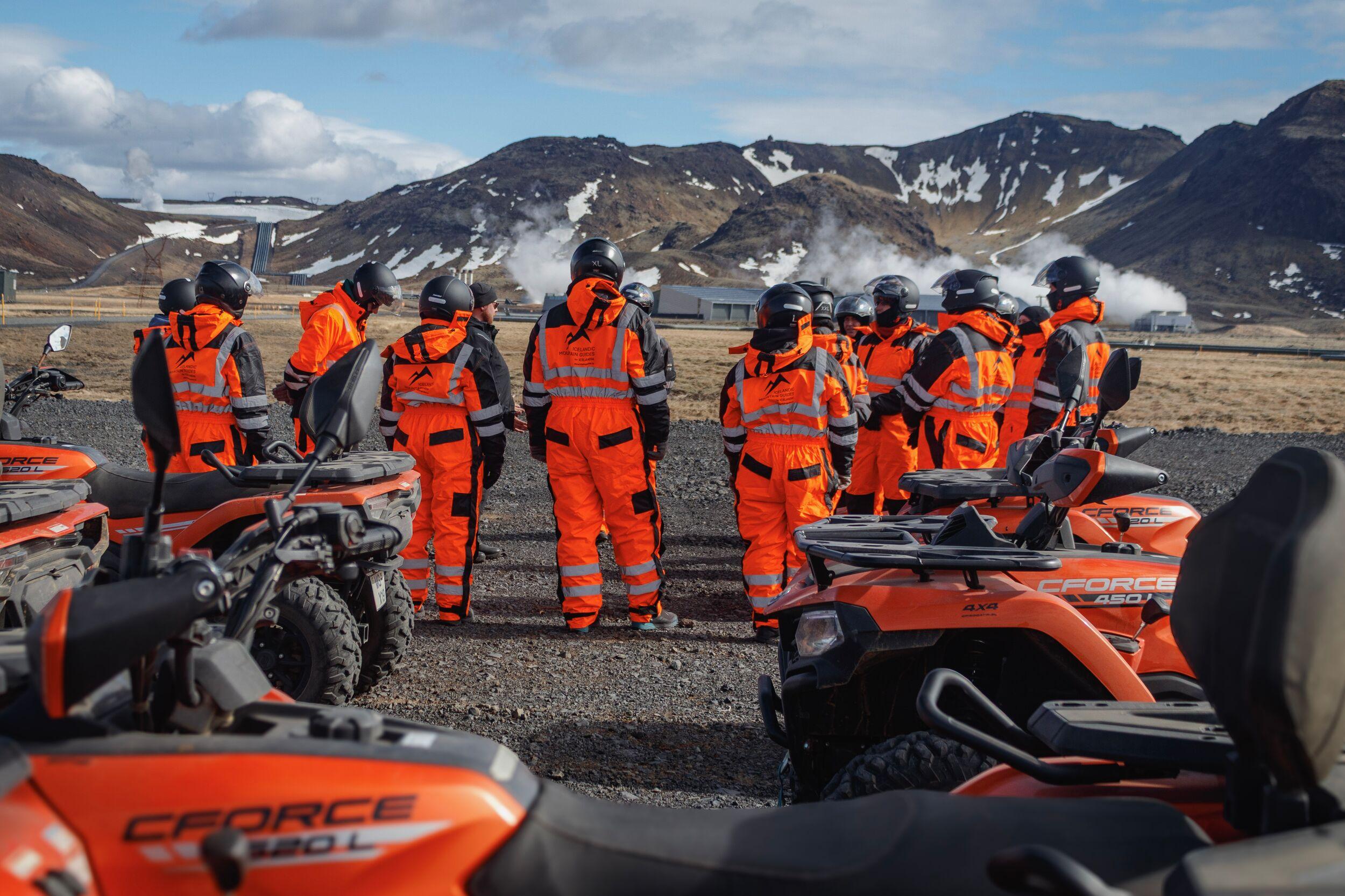 Group of people standing beside an ATV, looking out over a steaming geothermal area.