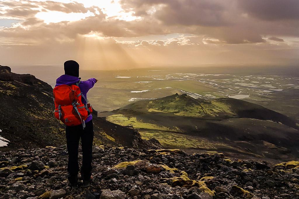 A female hiker standing on a viewpoint and pointing towards the sunset