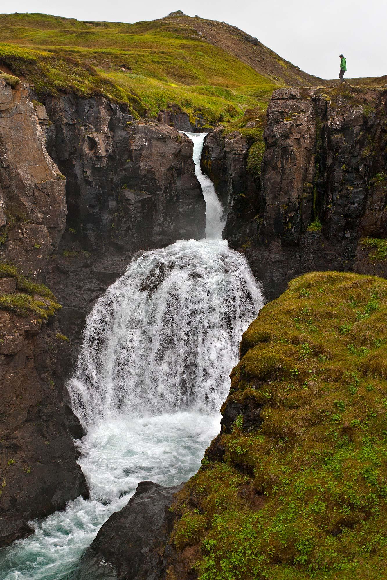 A man looking down at a waterfall from a cliff in icelandic nature