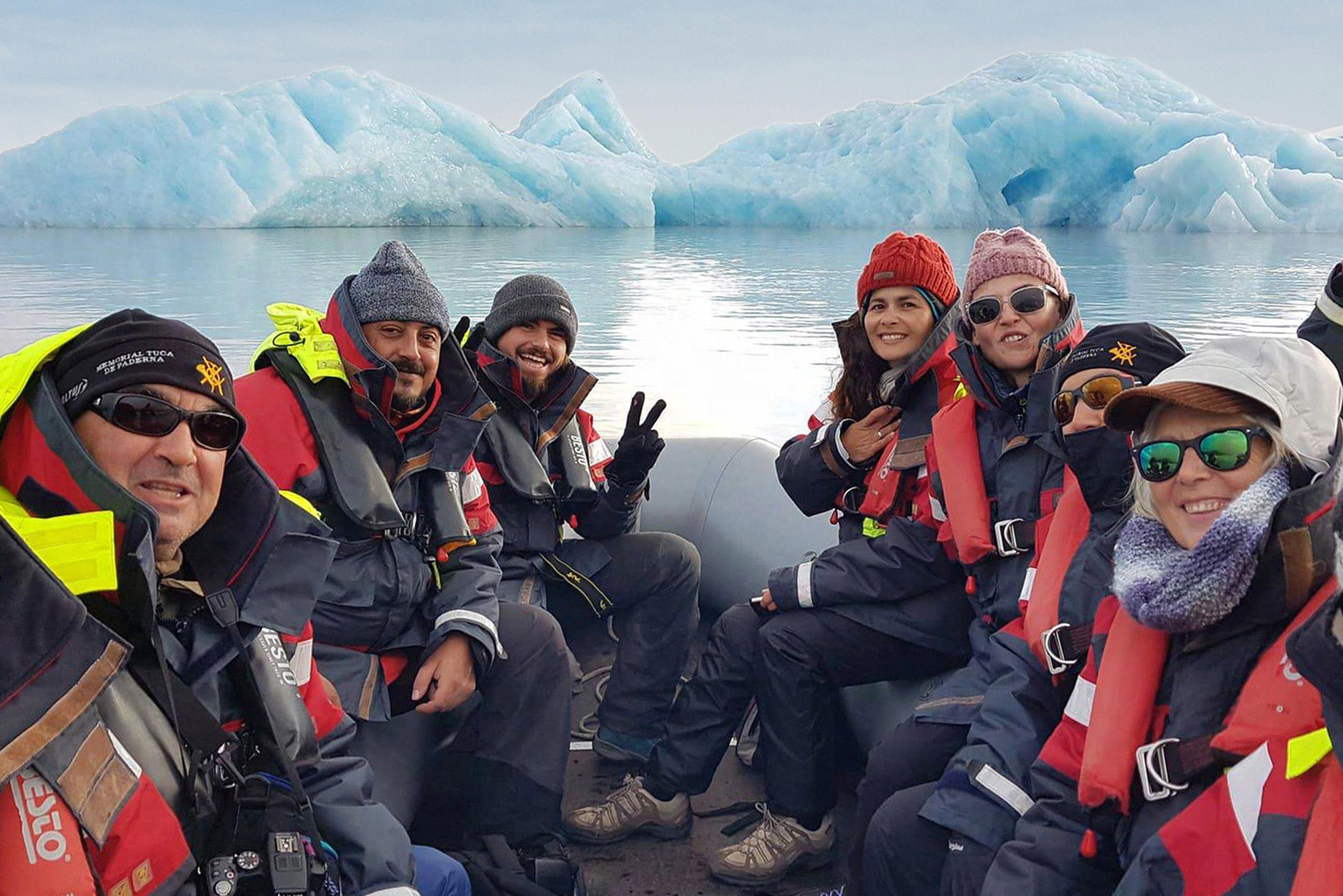 Six people in a boat on a glacier lagoon with blue icebergs behind them.
