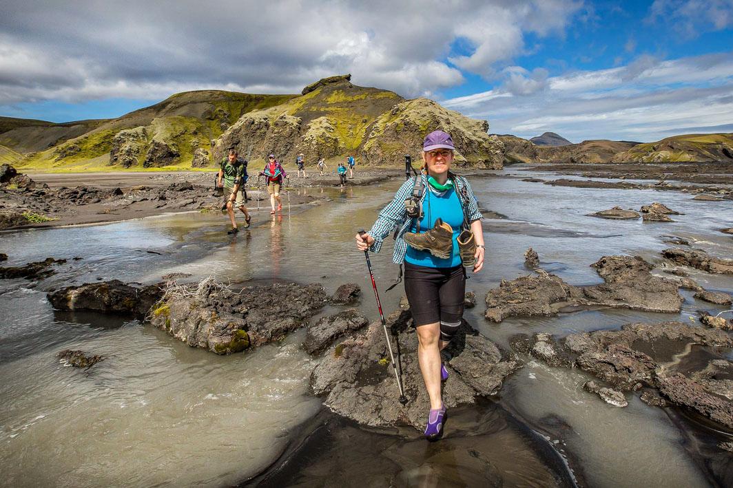 Hikers crossing a shallow river in a beautiful landscape in sunny weather
