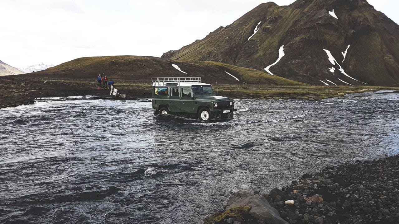 Land Rover crossing a river with a mountain in the background