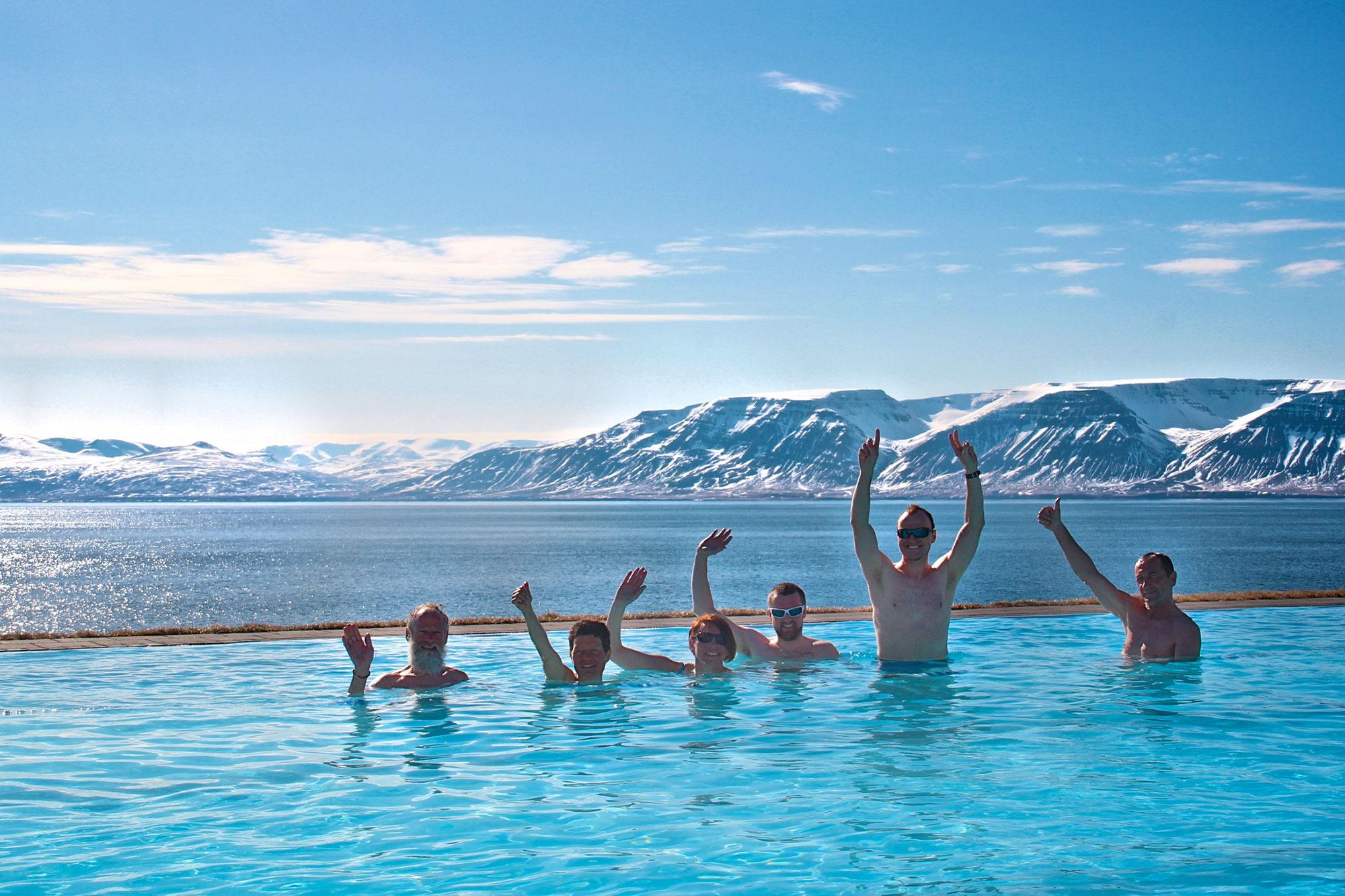 Happy people in a swimming pool with snowy mountains and a blue ocean behind them