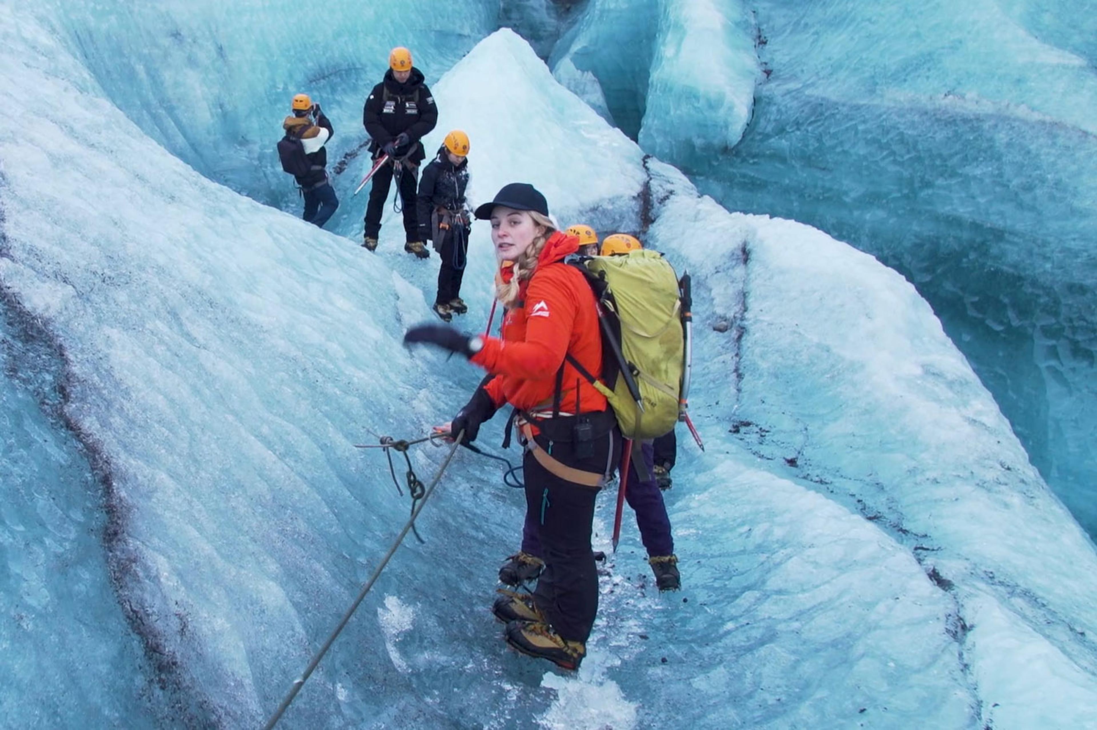 A woman guide dressed in a red jacket standing on a glacier guiding a glacier hike in Skaftafell in Vatnajokull National Park in Iceland.