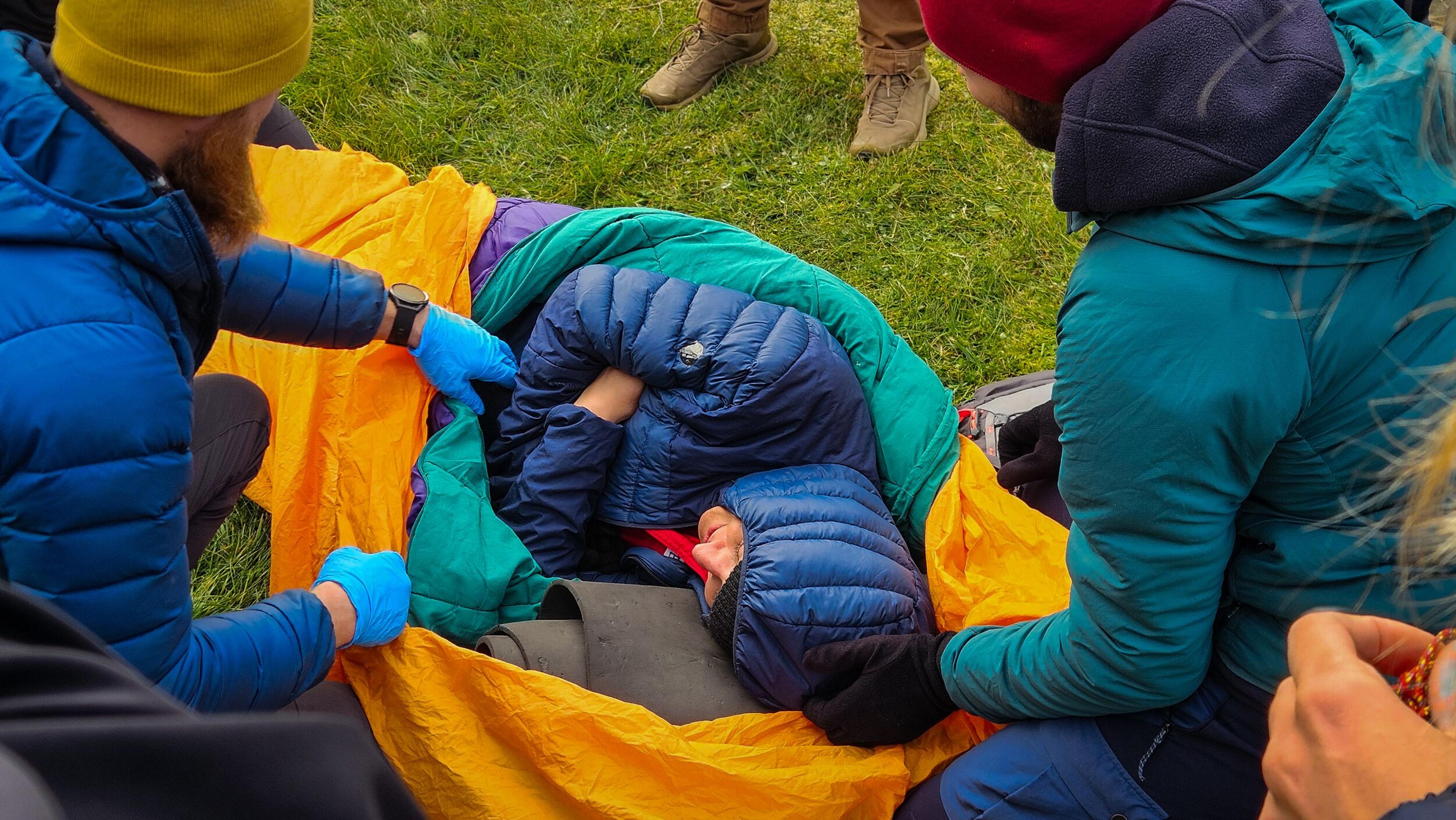 This image shows a group of people in a wilderness setting practicing a first responder or emergency care technique. 