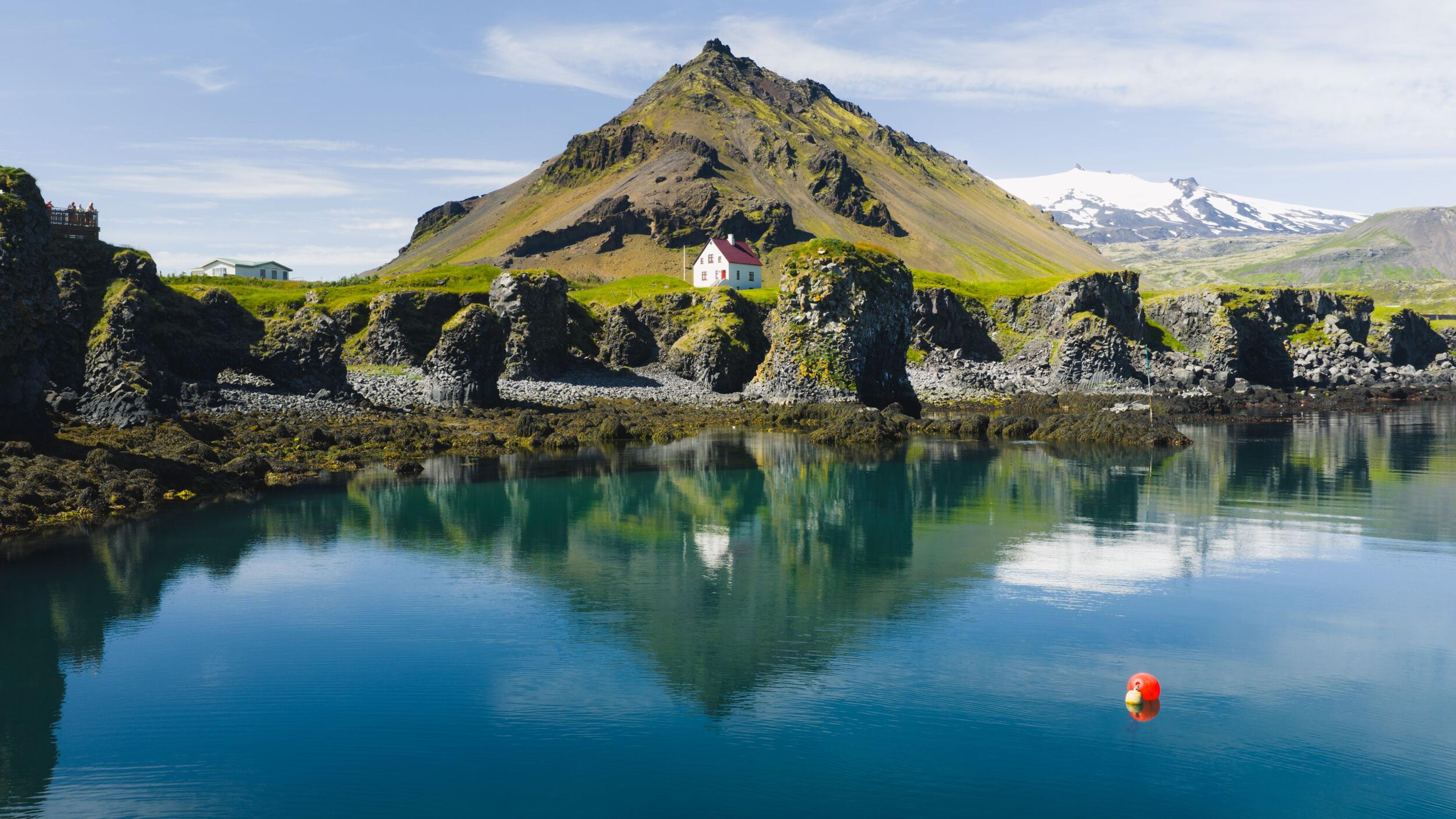 view over a mountain and a white house by cliffs by the shore.