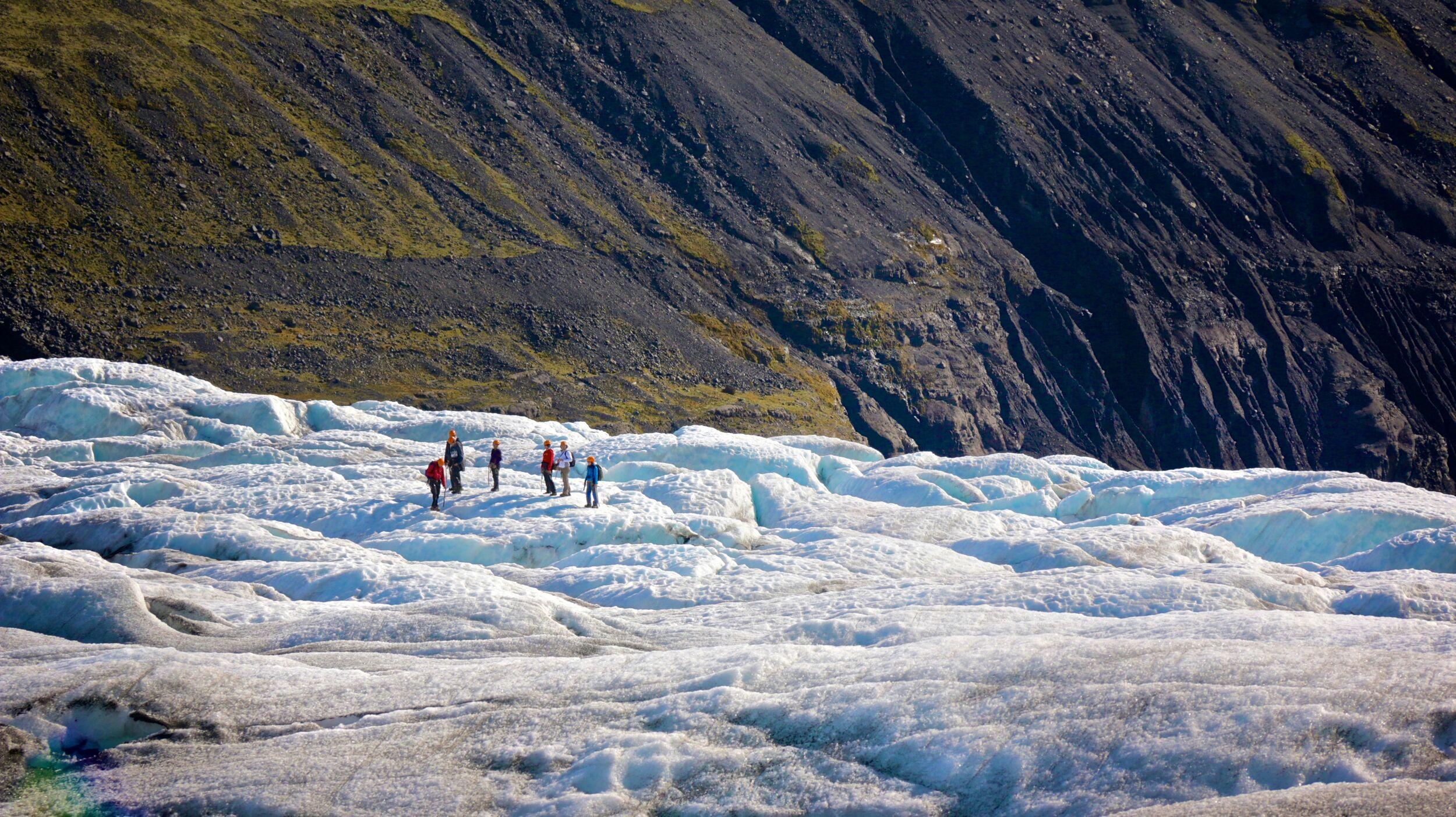 Small group trekking across Sólheimajökull glacier, surrounded by ice and rugged terrain.