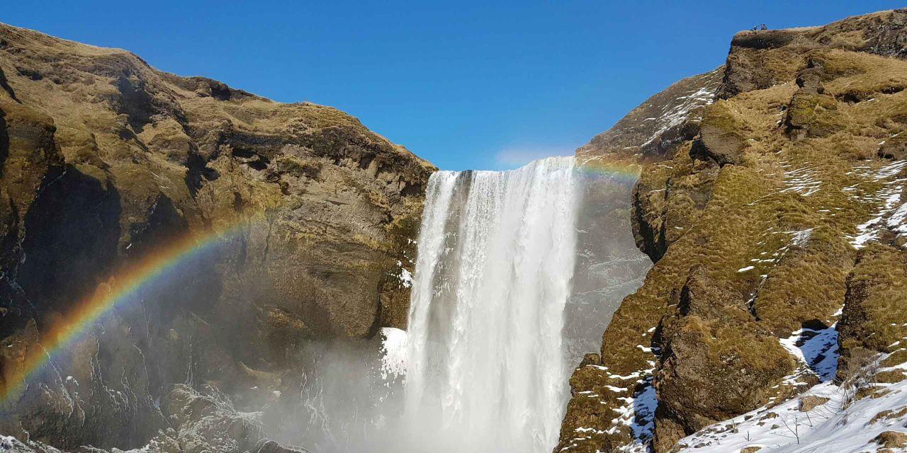 A picture of Skógafoss with a rainbow next to it