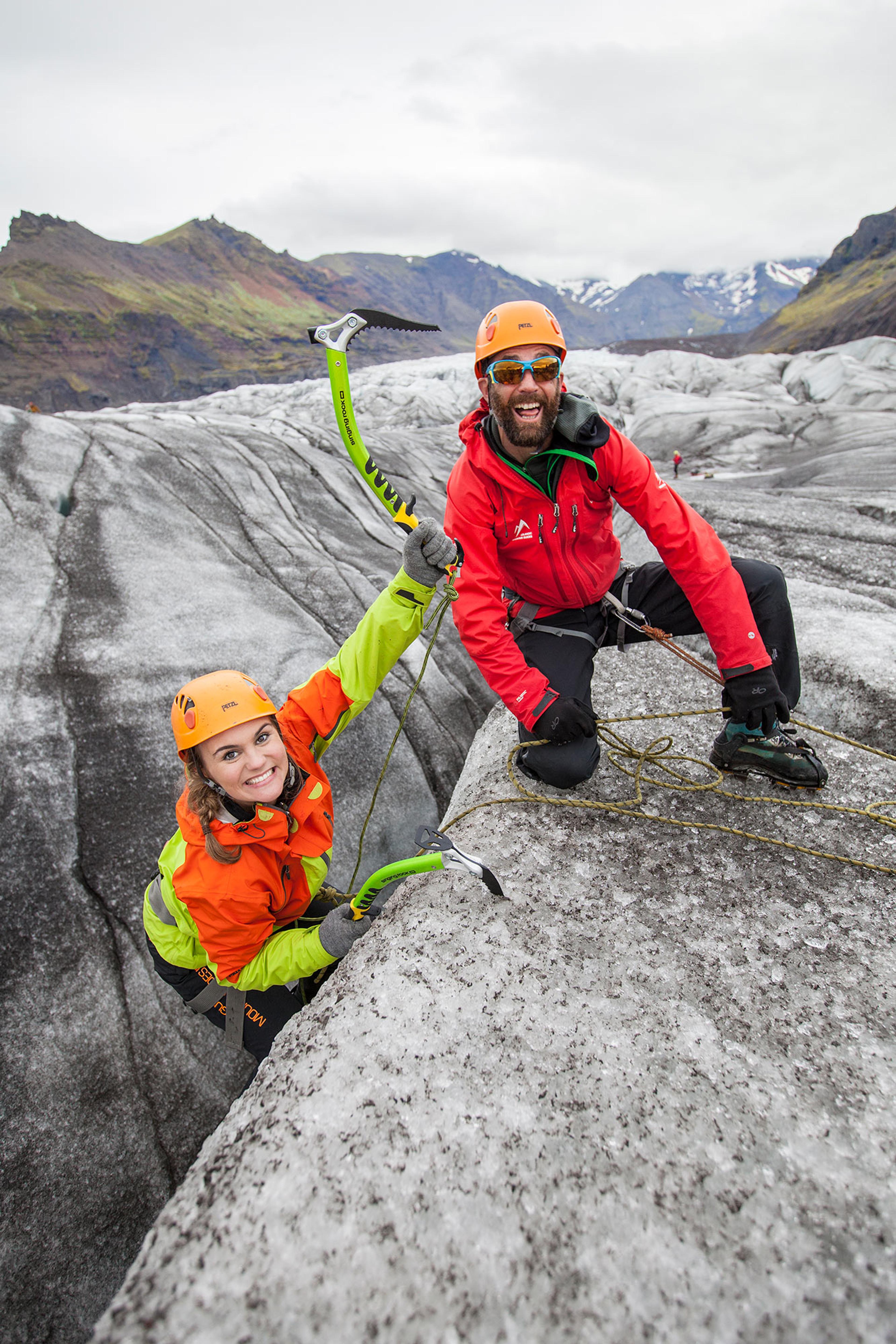 A climber in a yellow helmet and blue jacket steadies herself with a rope in an icy crevasse during a glacier climbing experience.