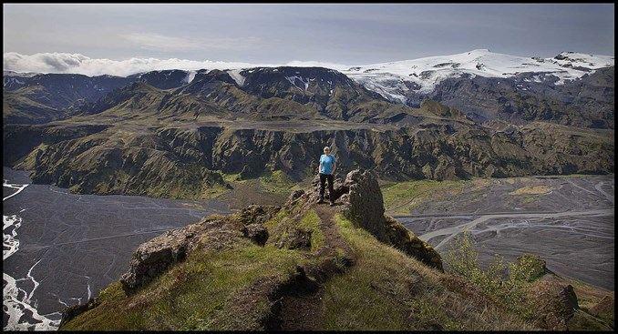 A woman standing in a mountain peak with more mountains in the back and rivers