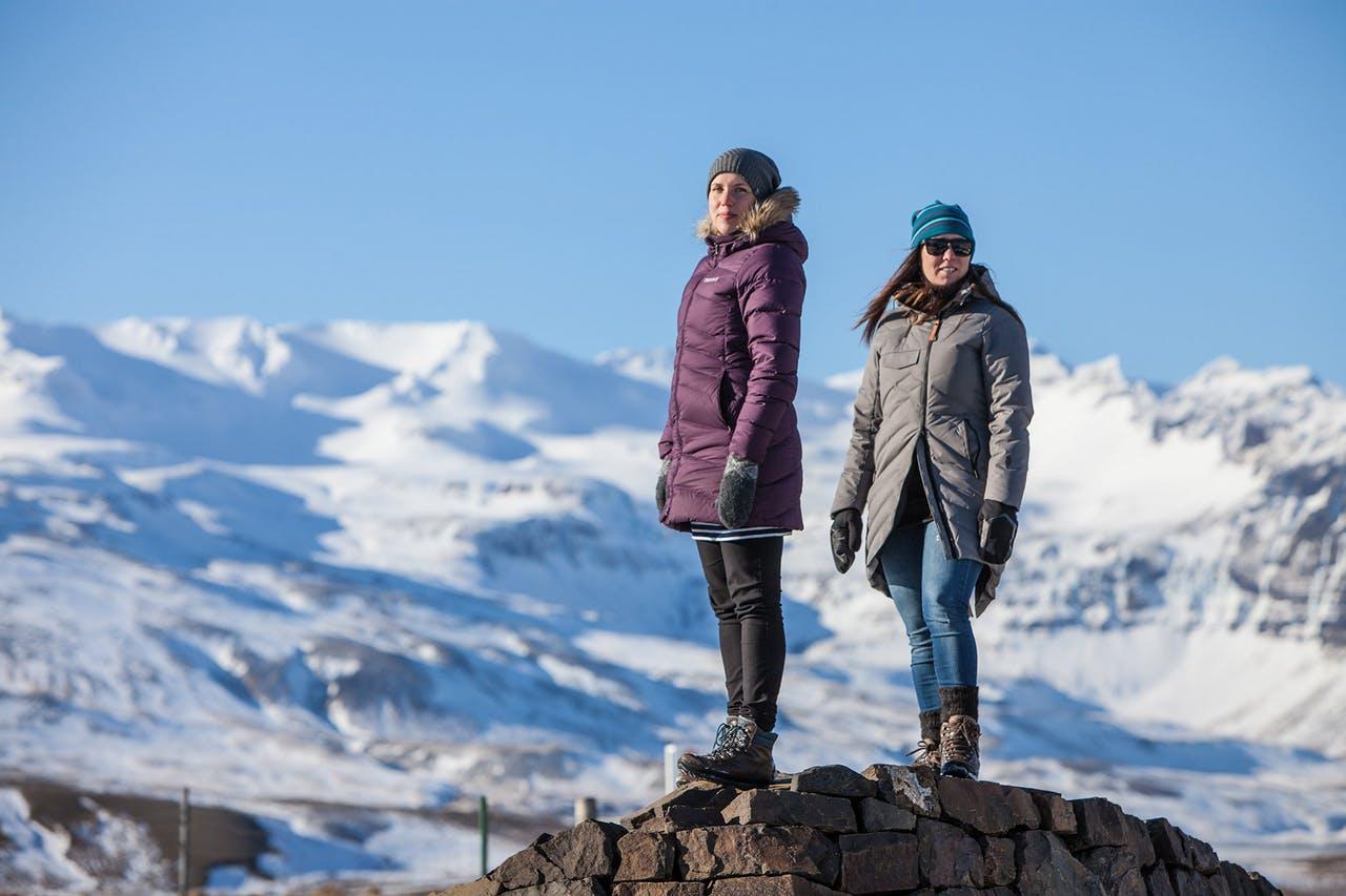 Tow women standing on top of a rock with snowy mountains in the background on a tour on Snaefellsnes peninsula  in February