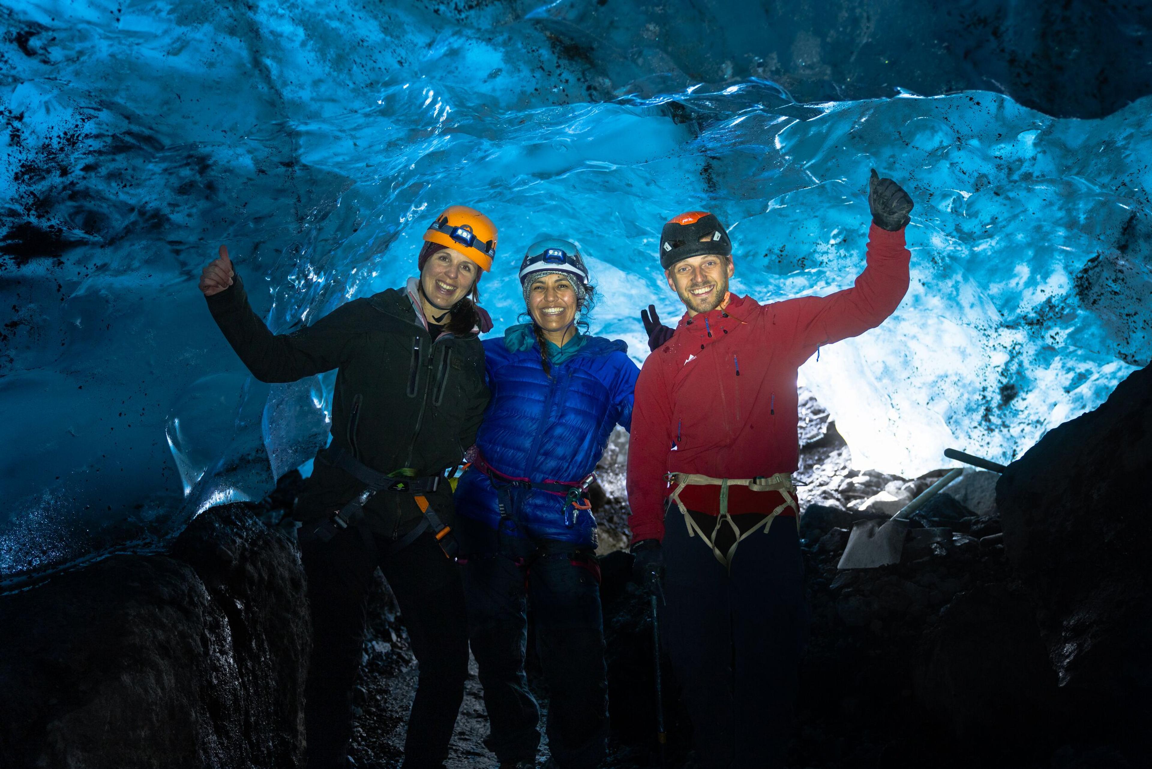 Three persons standing in an ice cave smiling