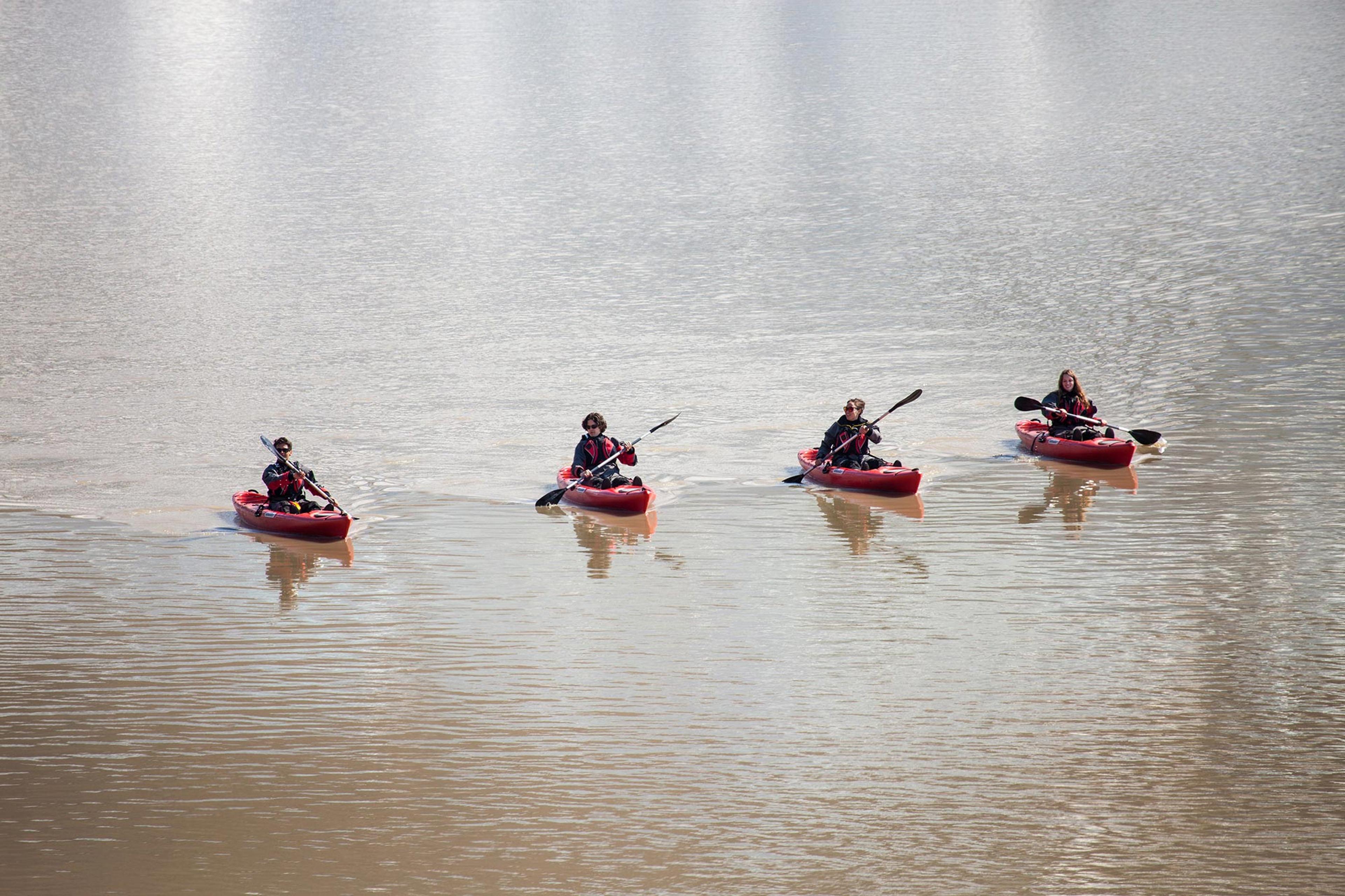 Four people in red kayaks paddling among giant icebergs side by side on Solheimajokull’s smooth glacier lagoon.