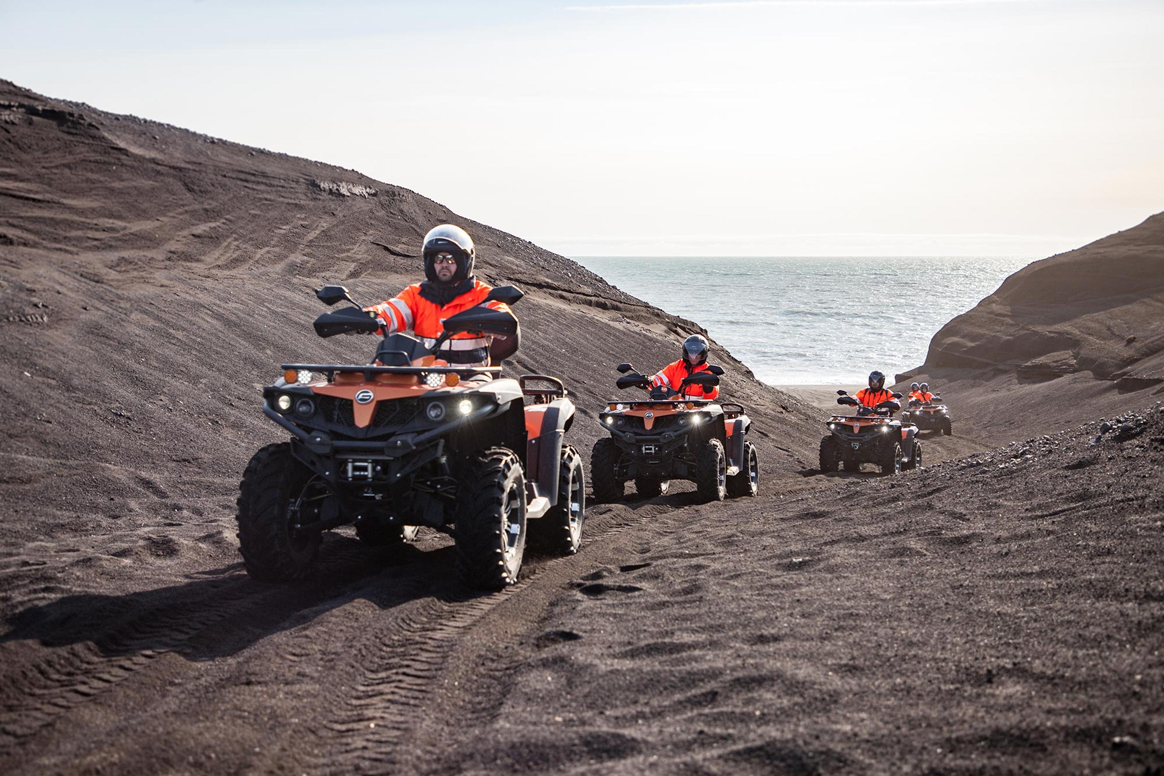 The group of ATV quad bike riders going in between black sand dunes near the ocean