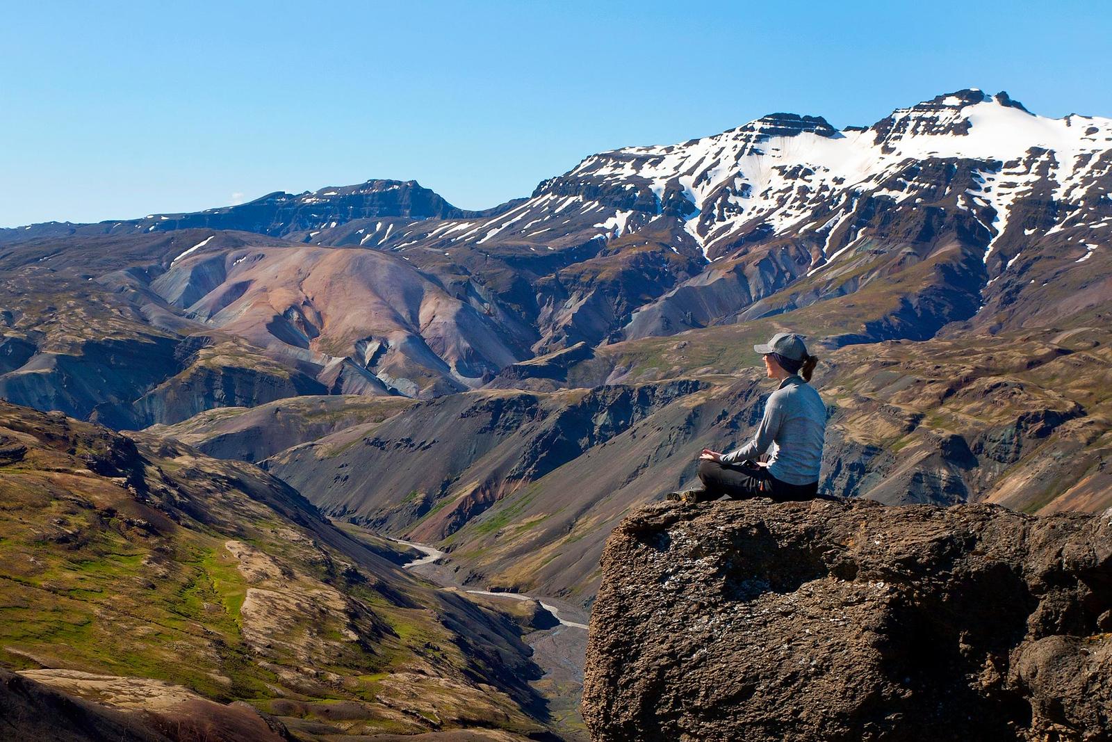 A woman sitting on a cliff admiring the view of beautiful big mountains near Vatnajökull in Iceland