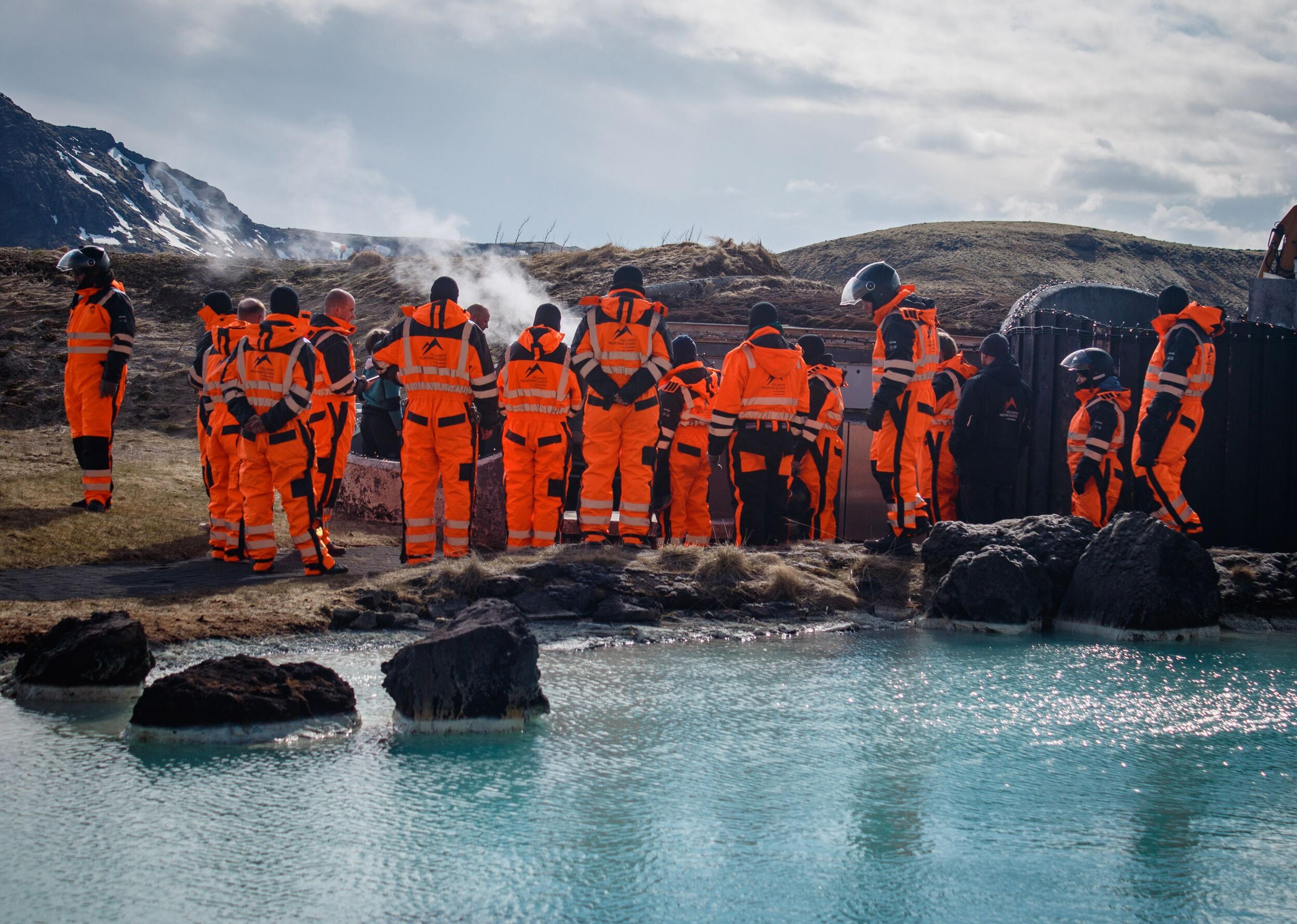 Group of people standing by a body of water with steam rising in the background.