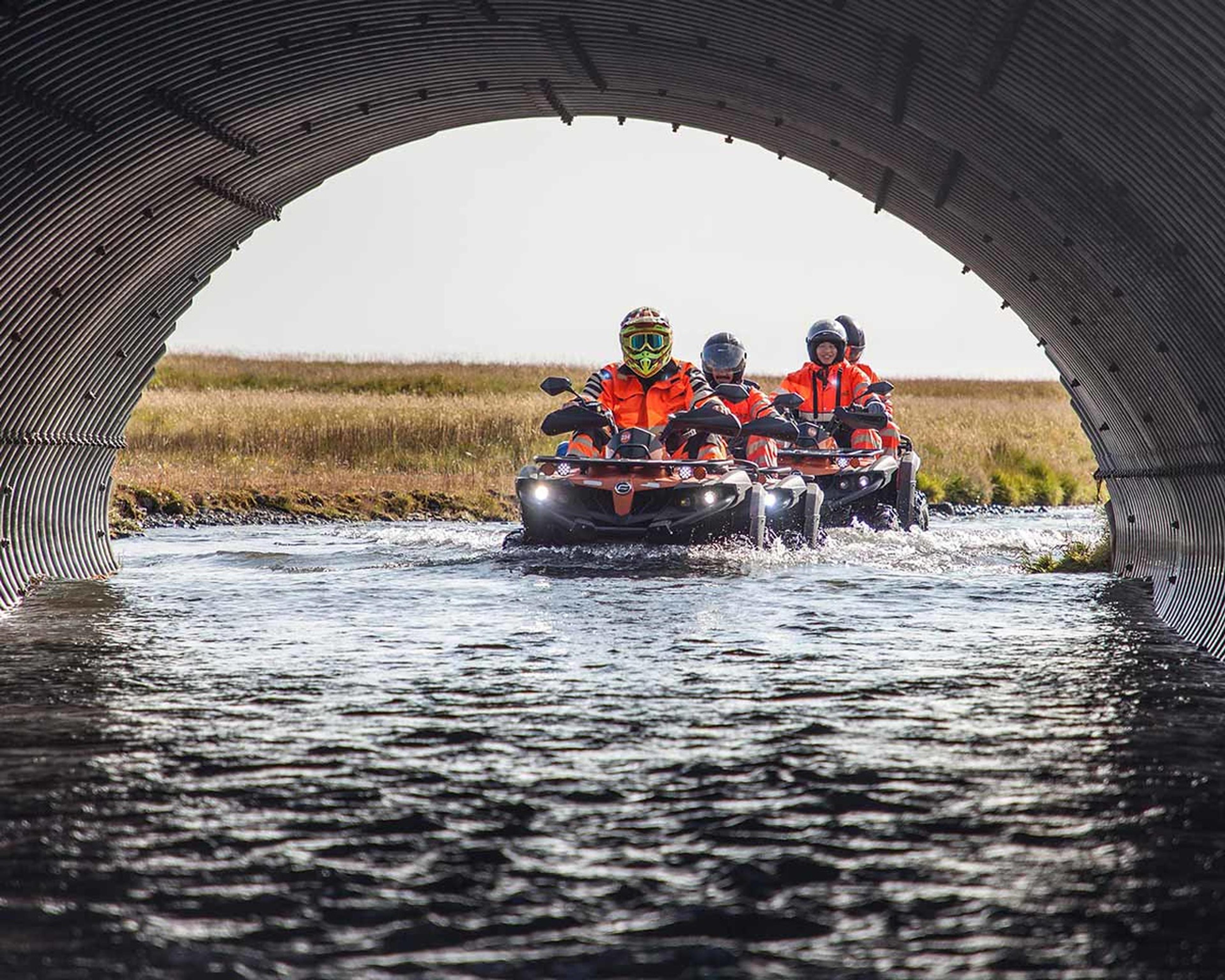 Riders on quad bikes going thorugh a water filled tube under the road