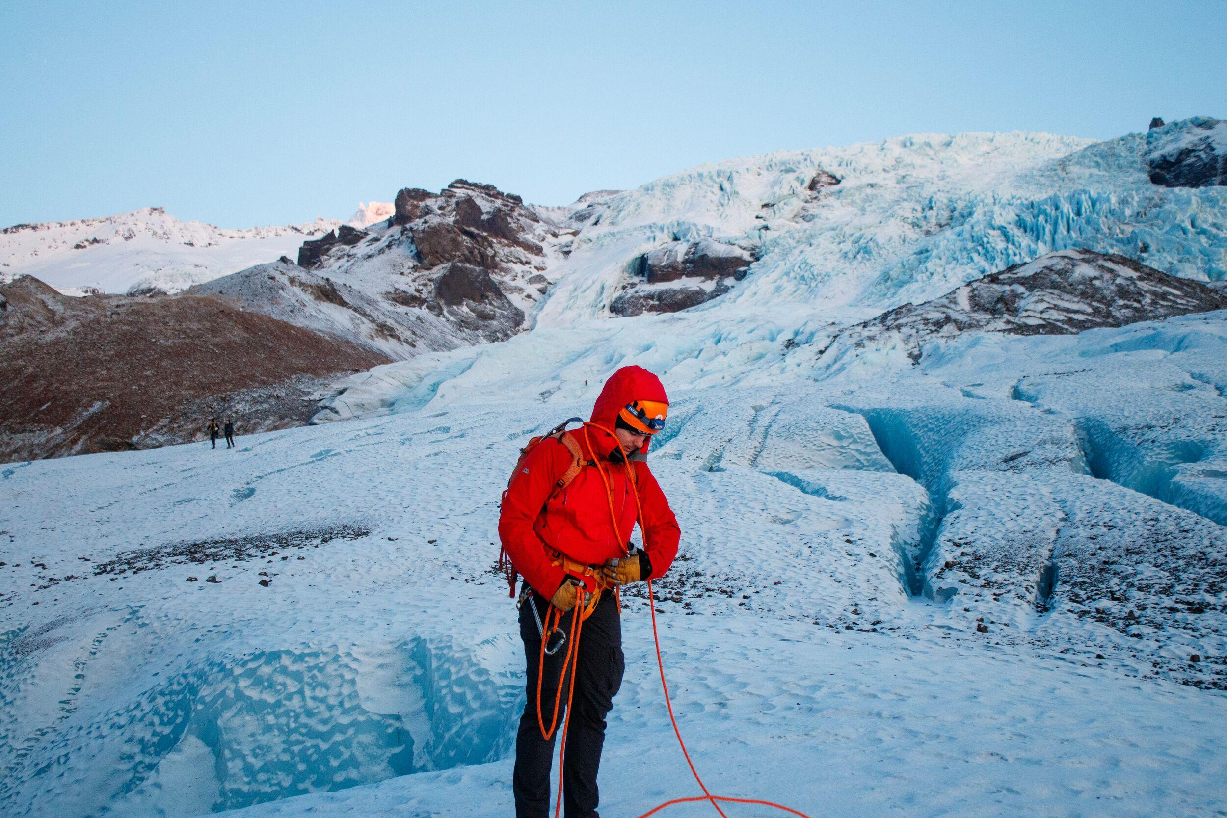 A hiker in a red jacket attaching a safety line on a glacier