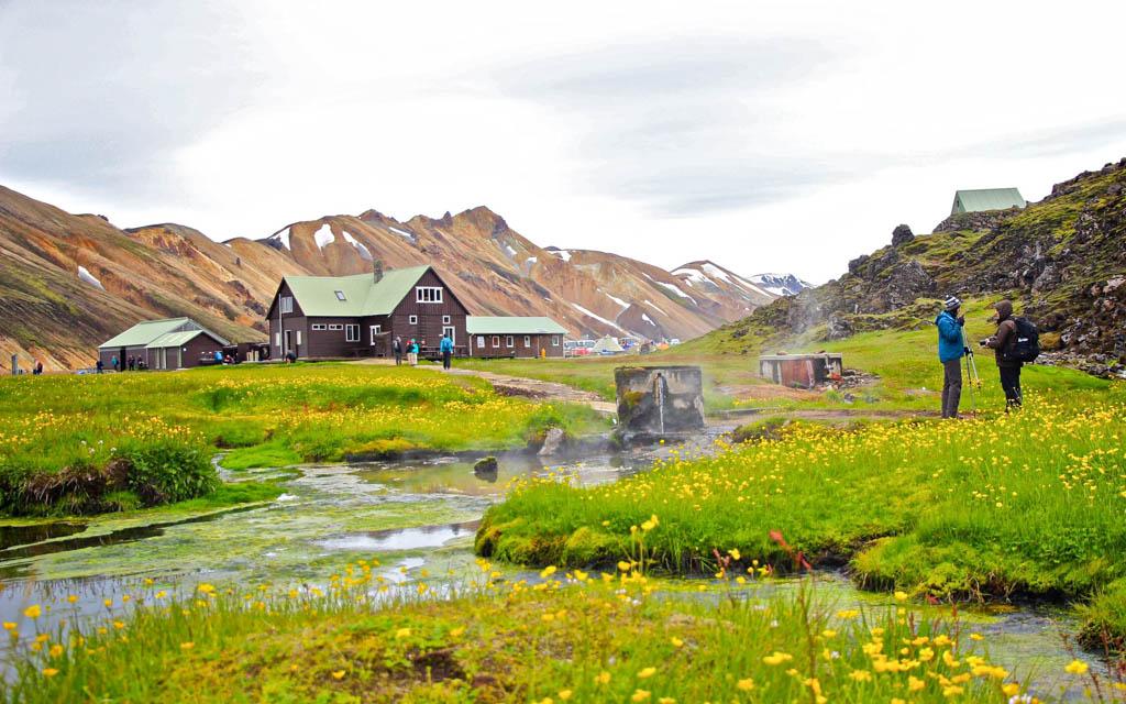 Hikers stand near hot springs and colorful buildings at Landmannalaugar base camp in Iceland.