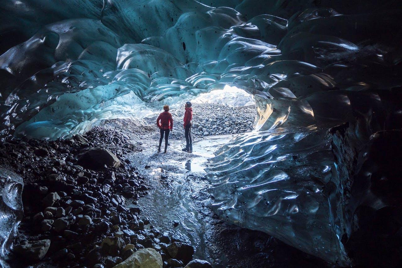 Two men in red standing in the opening of an Ice Cave in Iceland in February