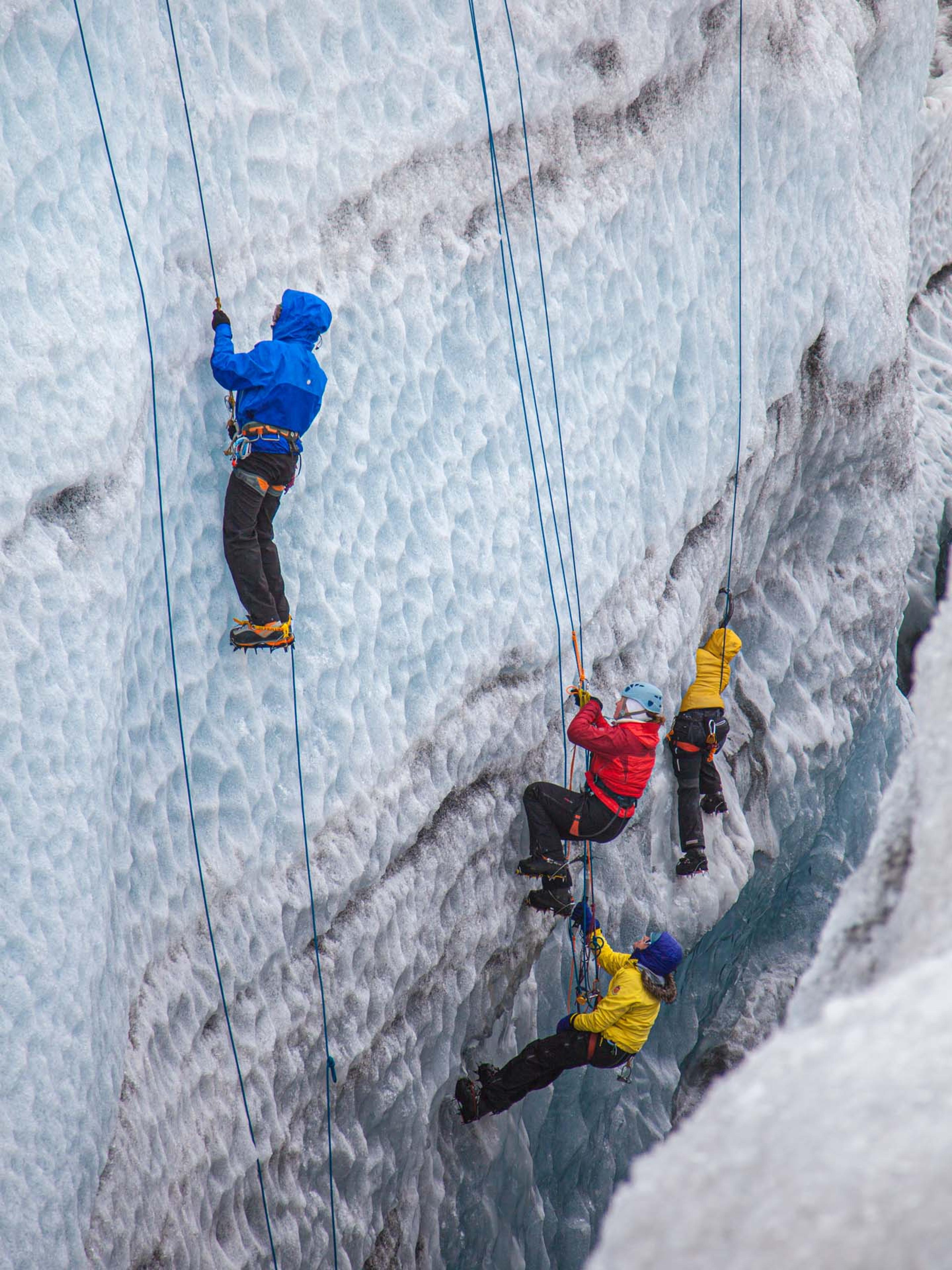 Four people ice climbing up a steep wall of ice