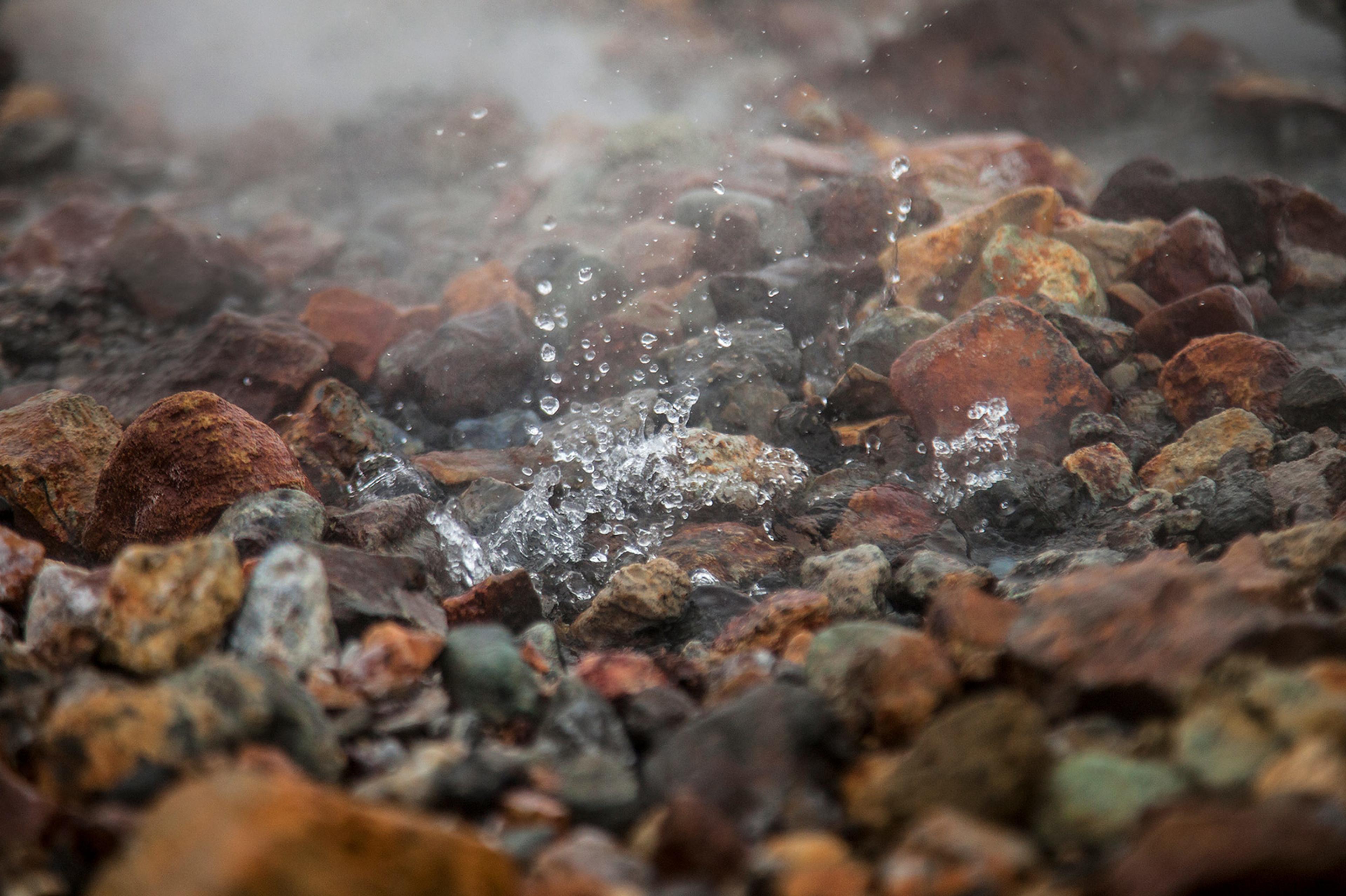 boiling water bubling up in between pebbles in a geothermal area