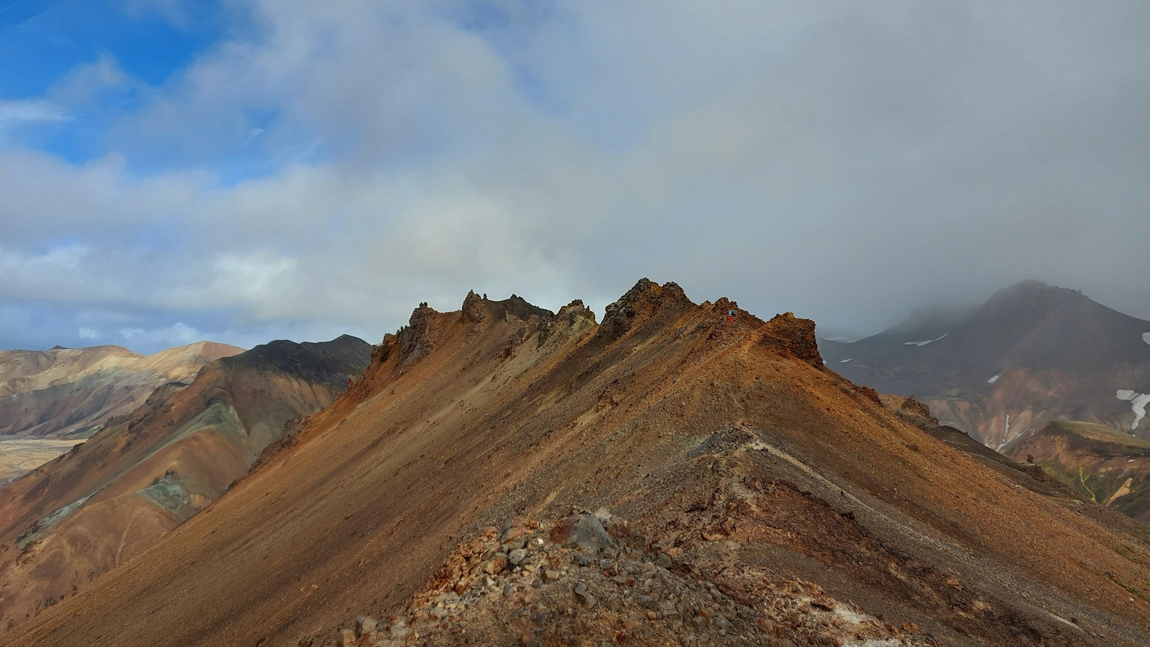 A sharp, rocky ridge stretches into the distance, contrasting the vibrant earth tones of Landmannalaugar's rugged terrain.