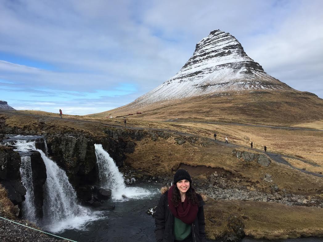 Sydney, Adventurer of the Week, is on Snæfellsnes peninsula posing for a photo in front of waterfall and Kirkjufell