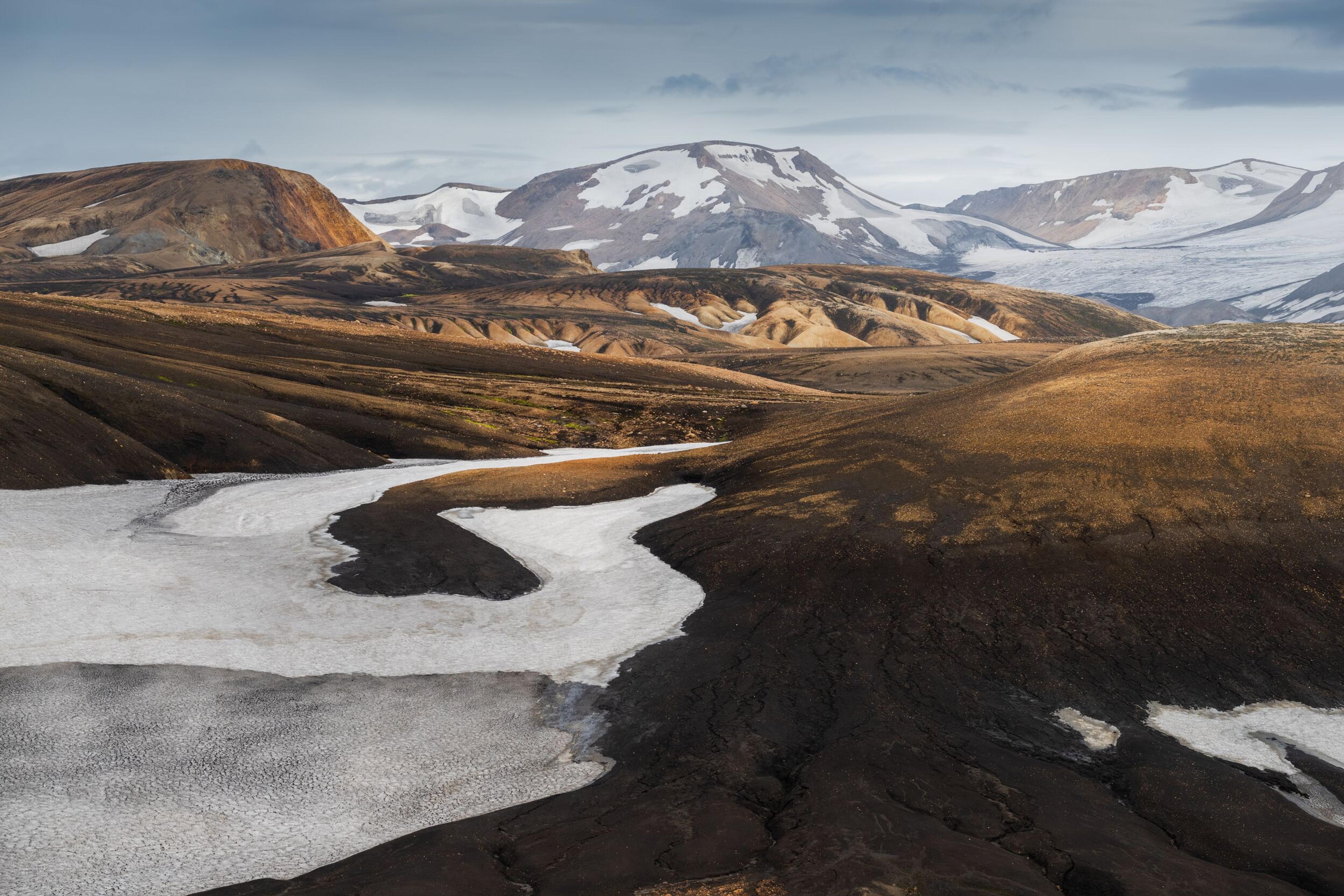 Hikers standing on the edge of a rugged, steep ridge in Landmannalaugar with rocky cliffs below.