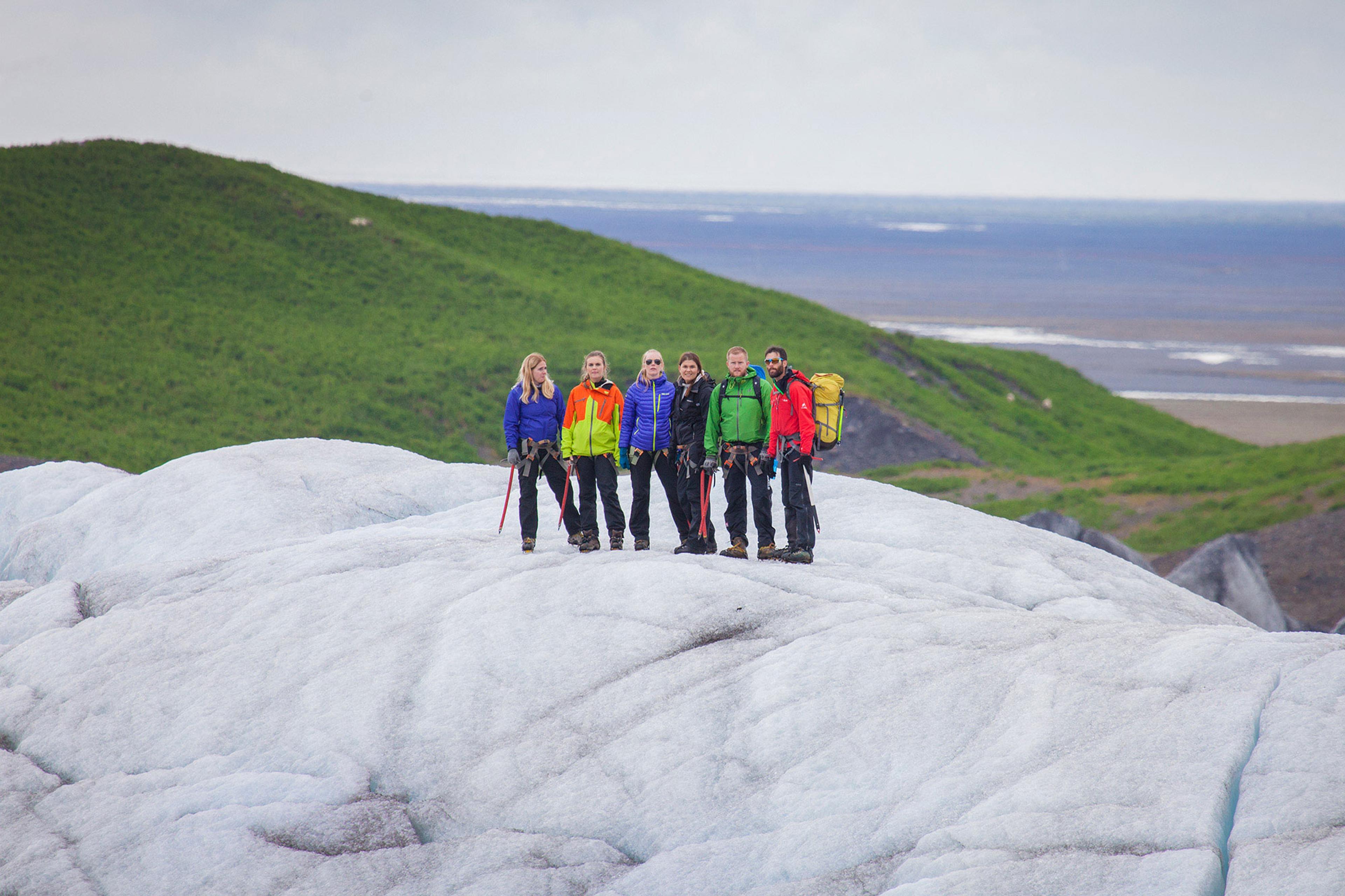 People on a glacier walk in Skaftafell with a vibrant green mountain behind them.
