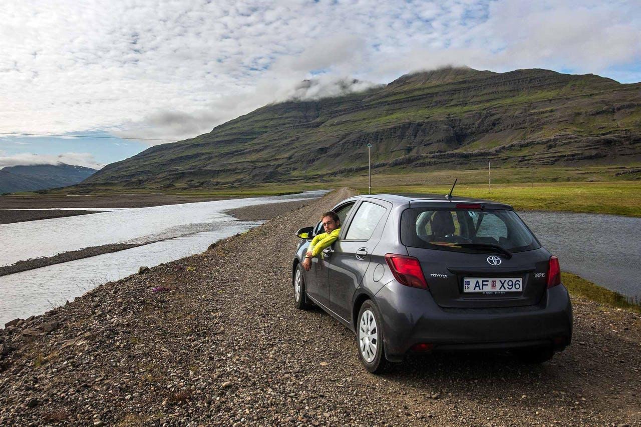 Man in a yellow jacket looking back out of the window of a black car on a dirt road in Iceland