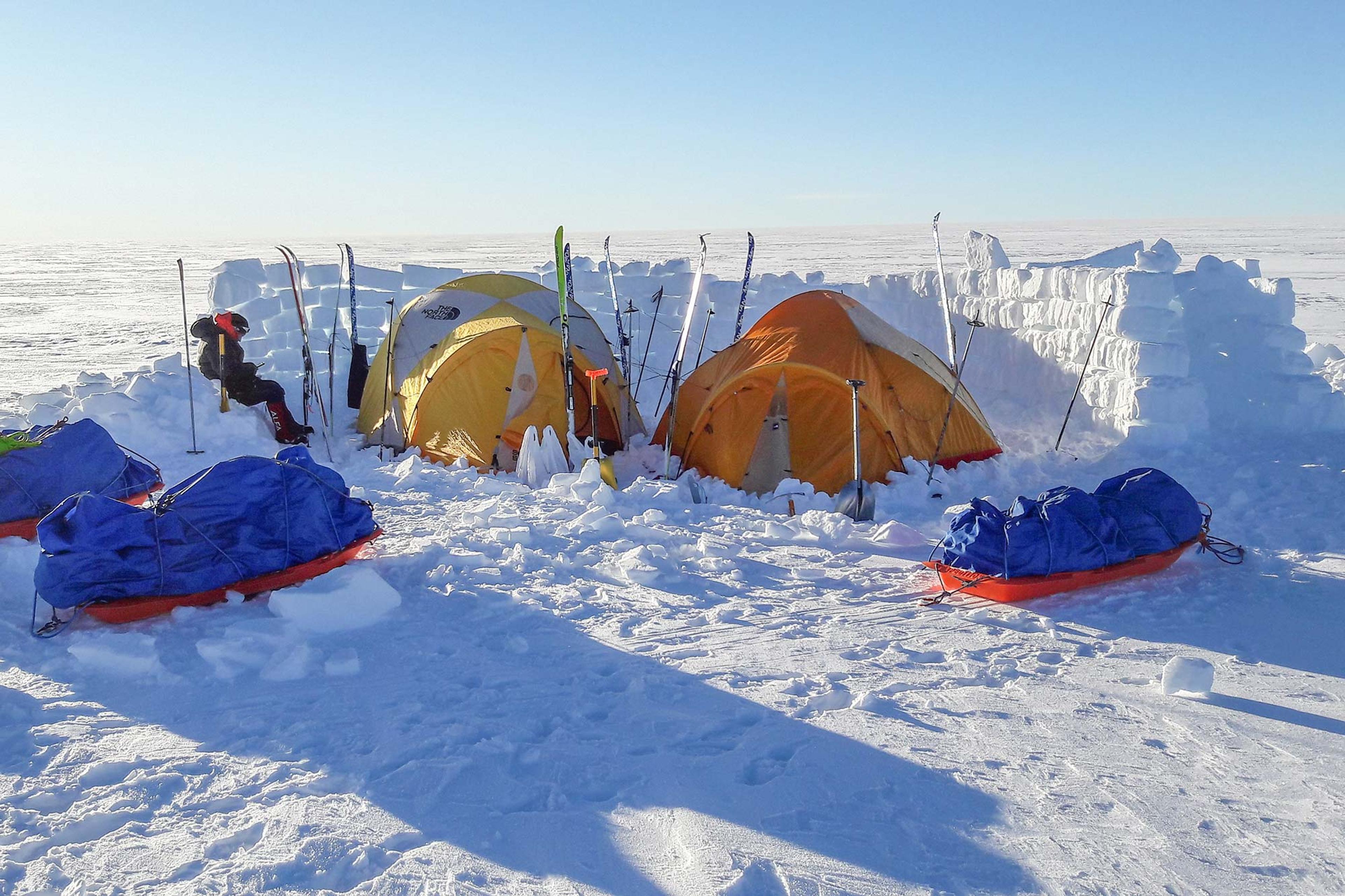 Two tends on the Greenland ice cap inside a snow wall and a man sitting by
