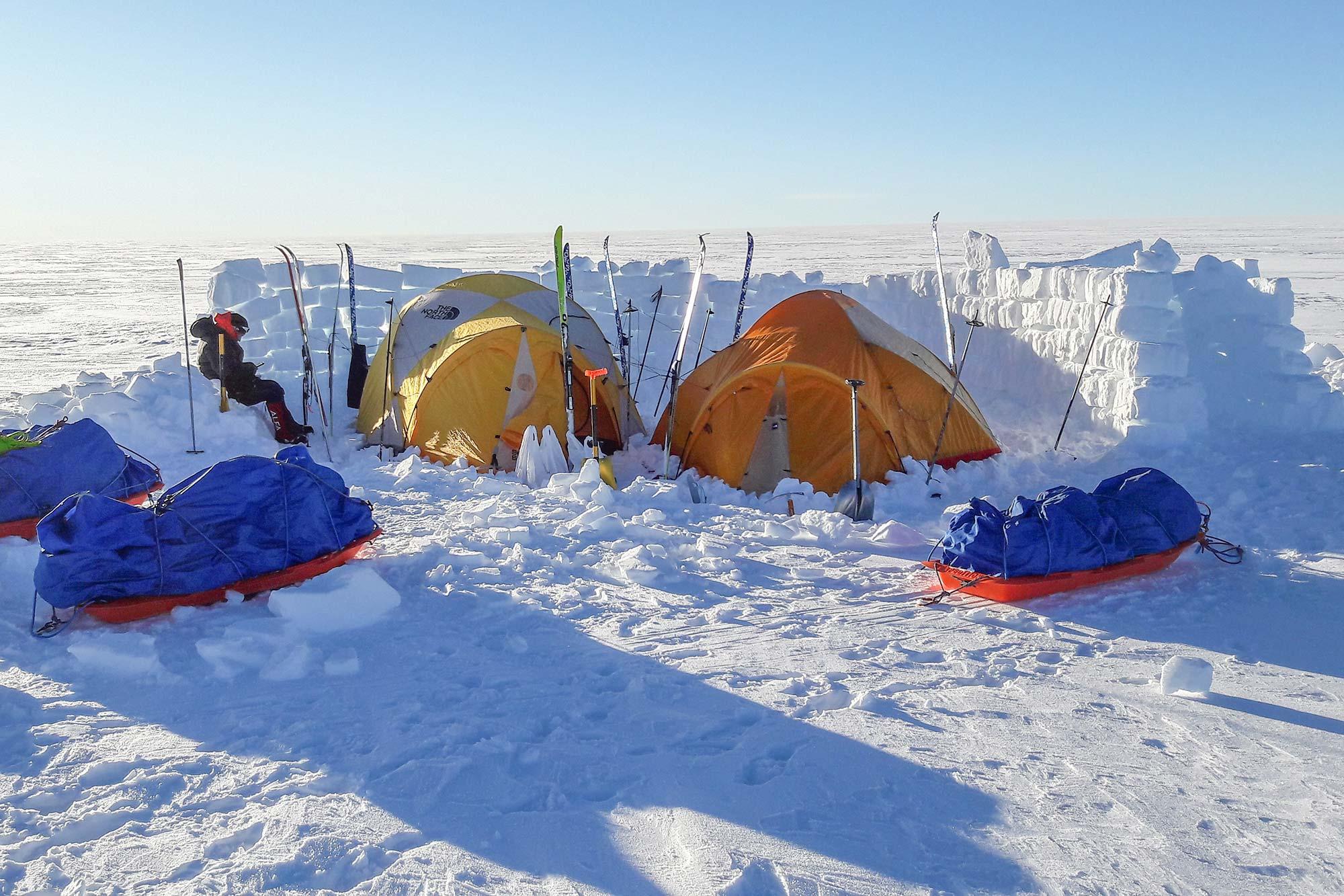 Two tends on the Greenland ice cap inside a snow wall and a man sitting by