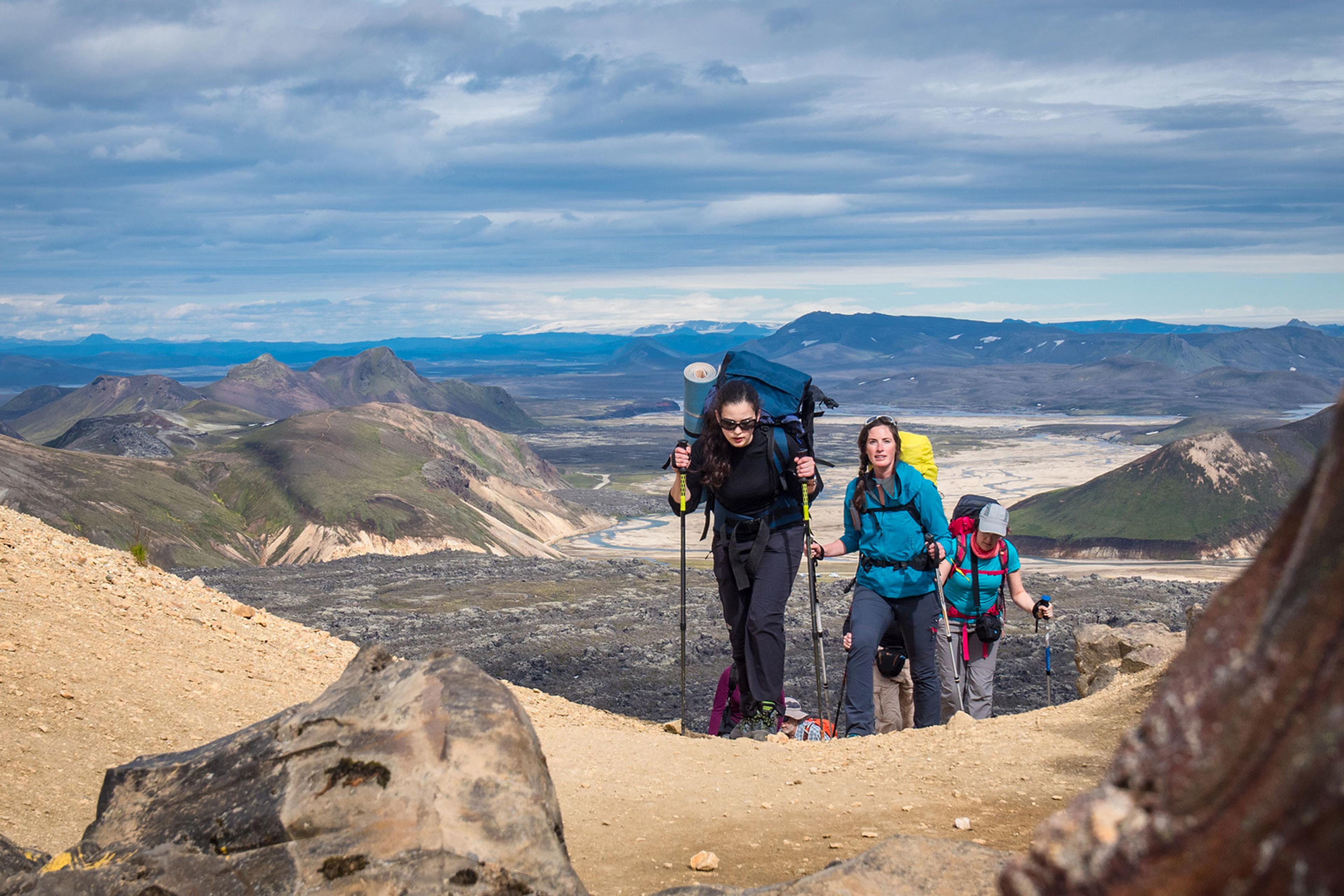 People hiking up a mountain on a sunny day on the Laugavegur trail with colorful mountains behind them