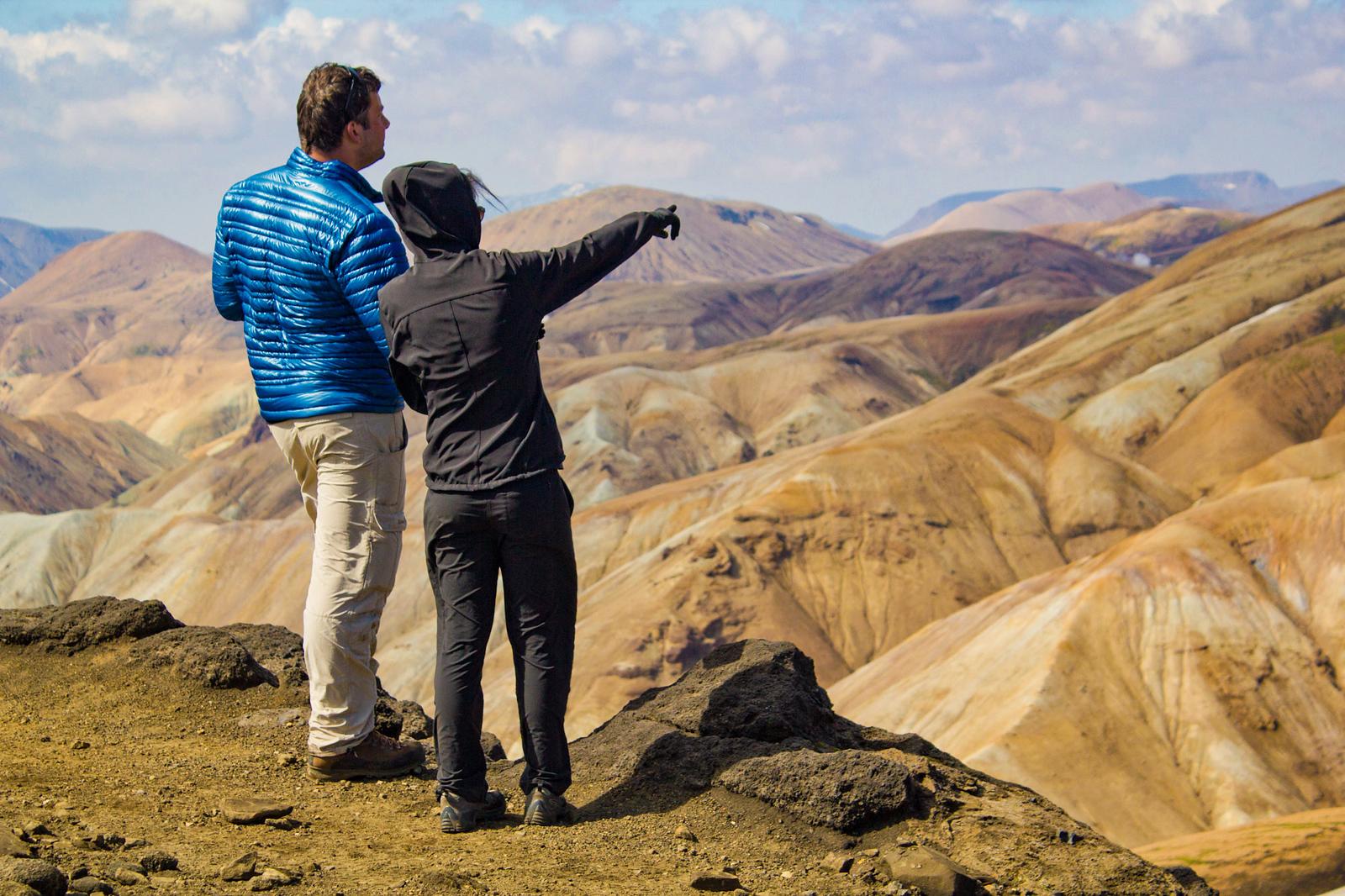 A couple admiring the veiw of yellow mountains from a cliff.